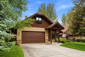 Stucco and wood-paneled exterior with stone accents, featuring an attached garage with a panel door, a covered entry, and a paved driveway