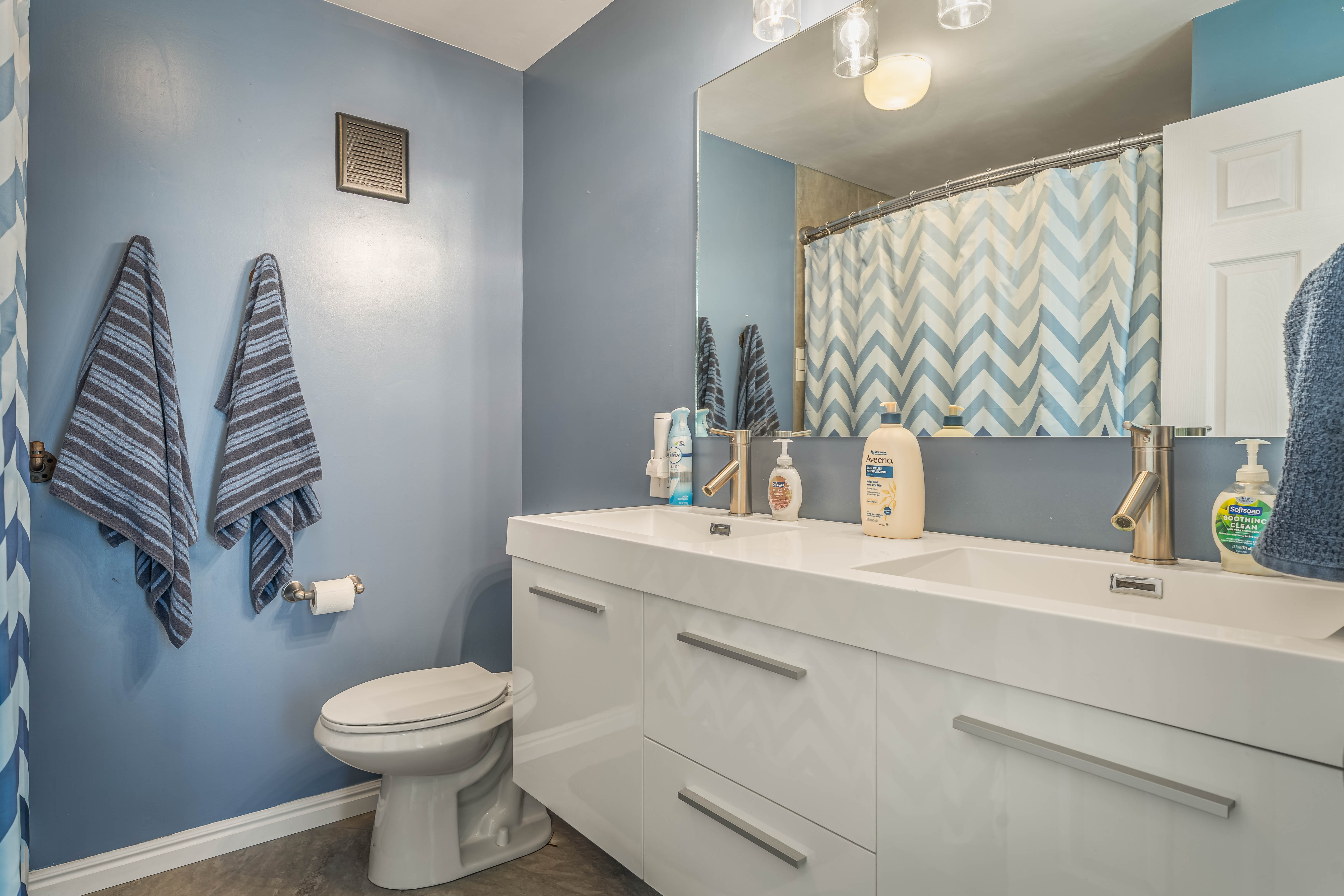 Bathroom featuring a dual vanity with white cabinetry and integrated sinks, brushed nickel faucets, and a large wall-mounted mirror
