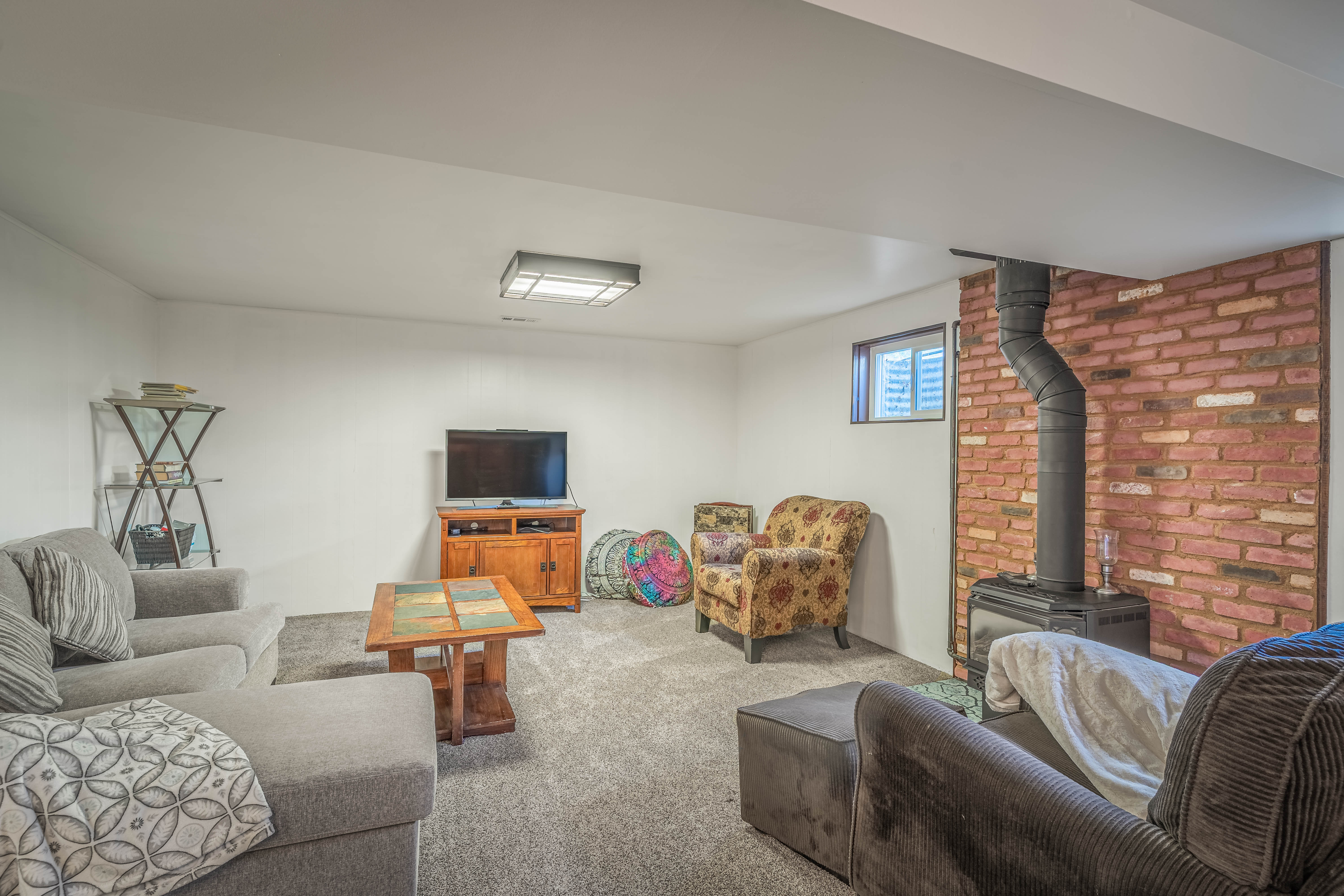 Living area featuring a textured gray carpet, recessed lighting, and a brick accent wall with a black wood-burning stove