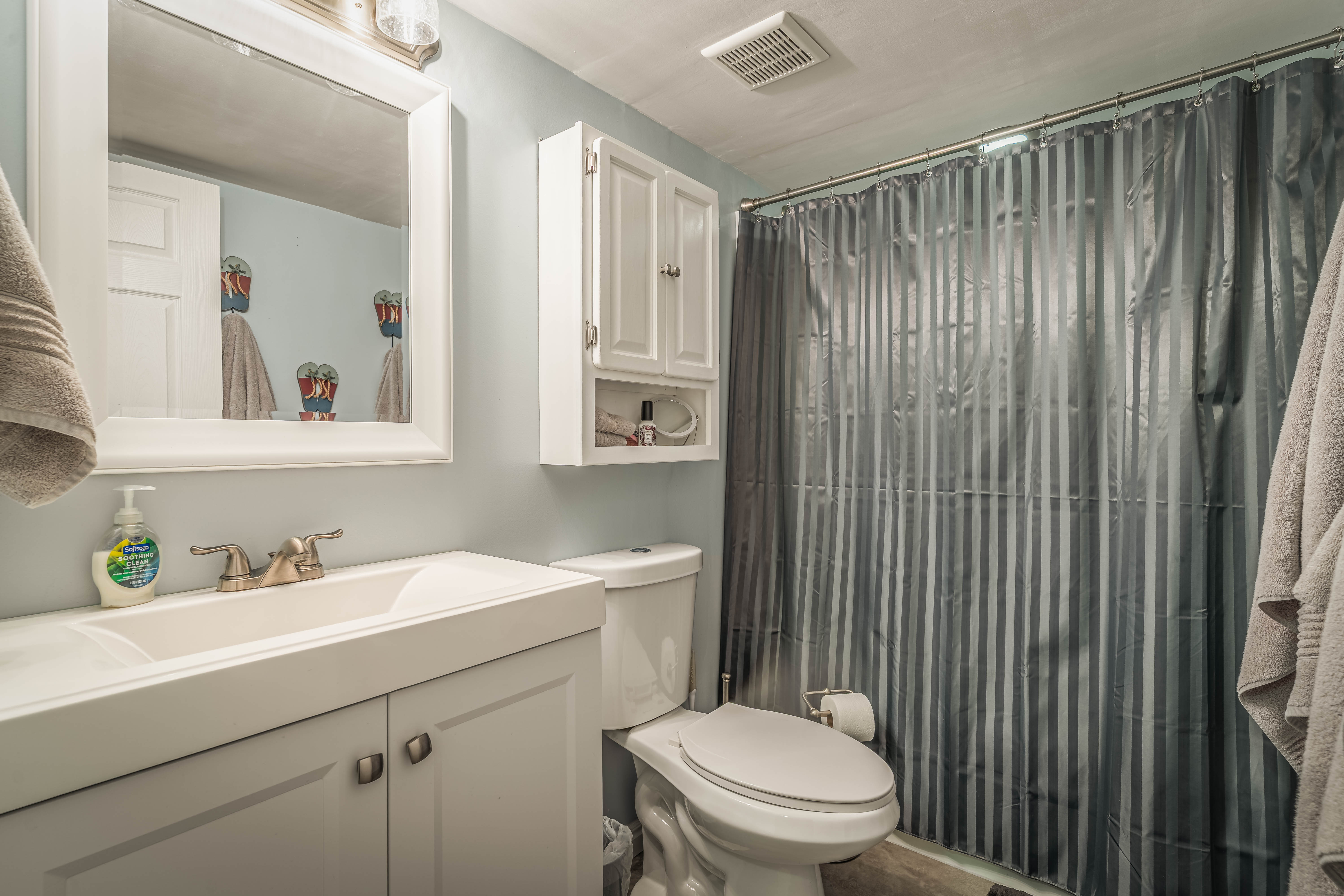 Bathroom featuring a white vanity with integrated sink, brushed nickel faucet, framed mirror, and a wall-mounted cabinet