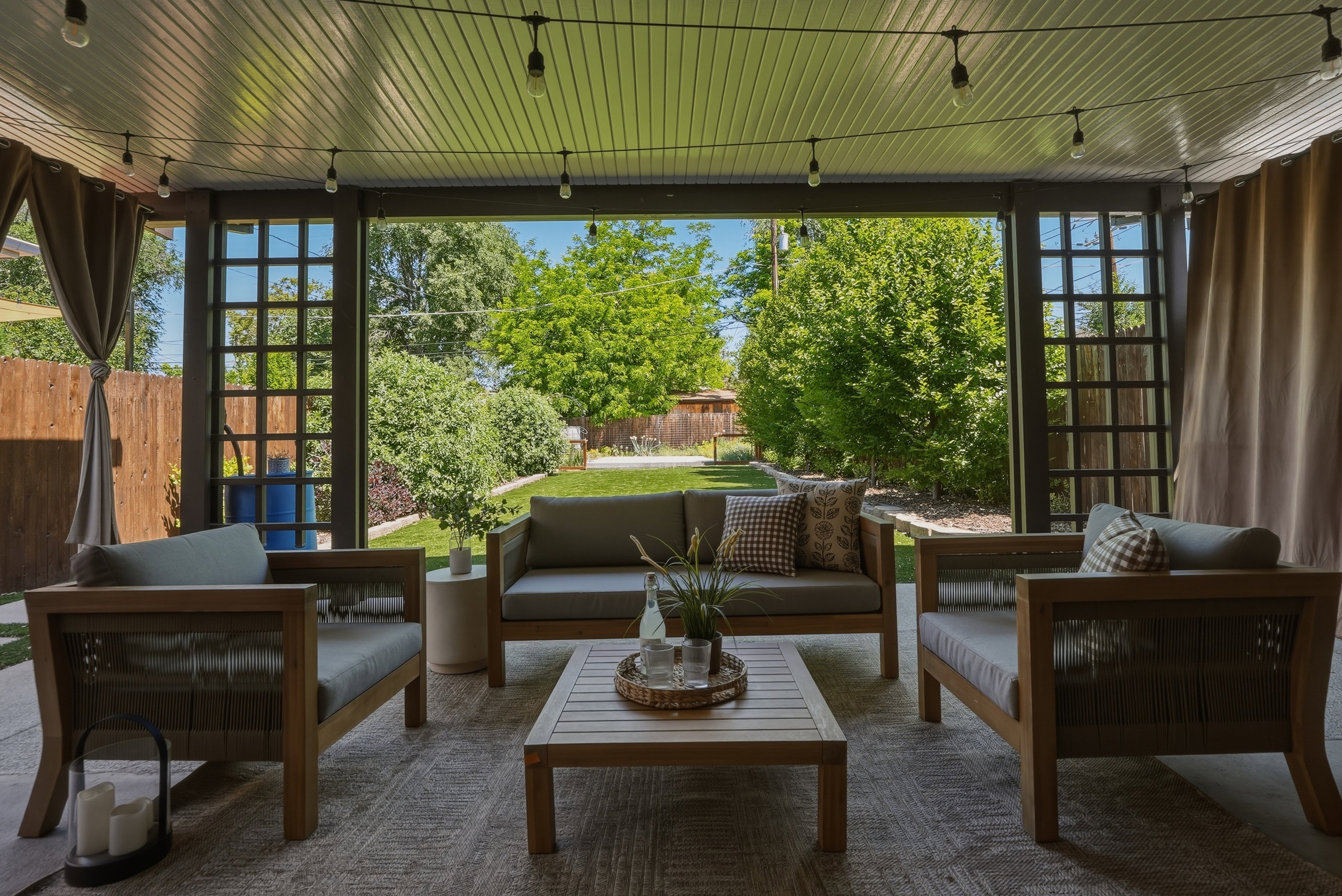 Covered patio featuring a slatted ceiling, string lighting, and privacy curtains