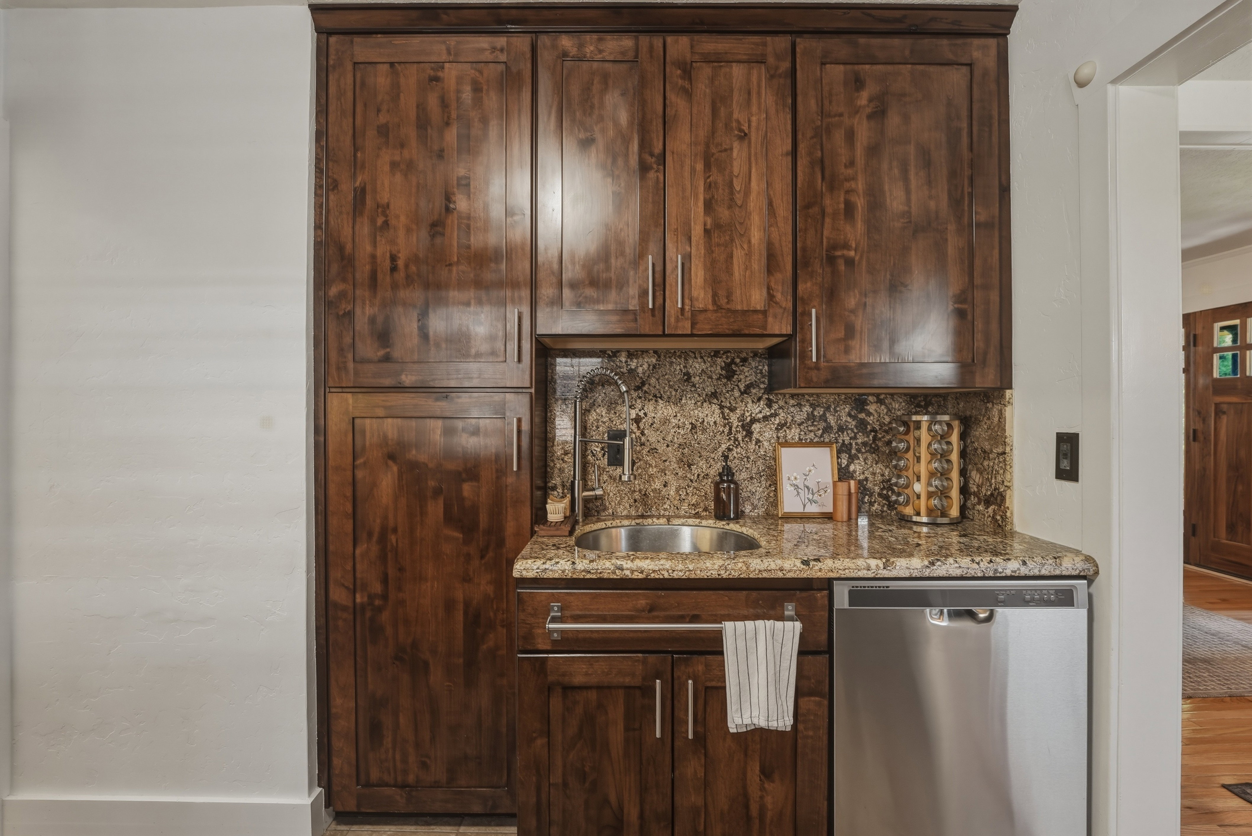 Custom dark wood-finish cabinetry featuring a built-in stainless steel dishwasher, undermount sink, and granite countertops