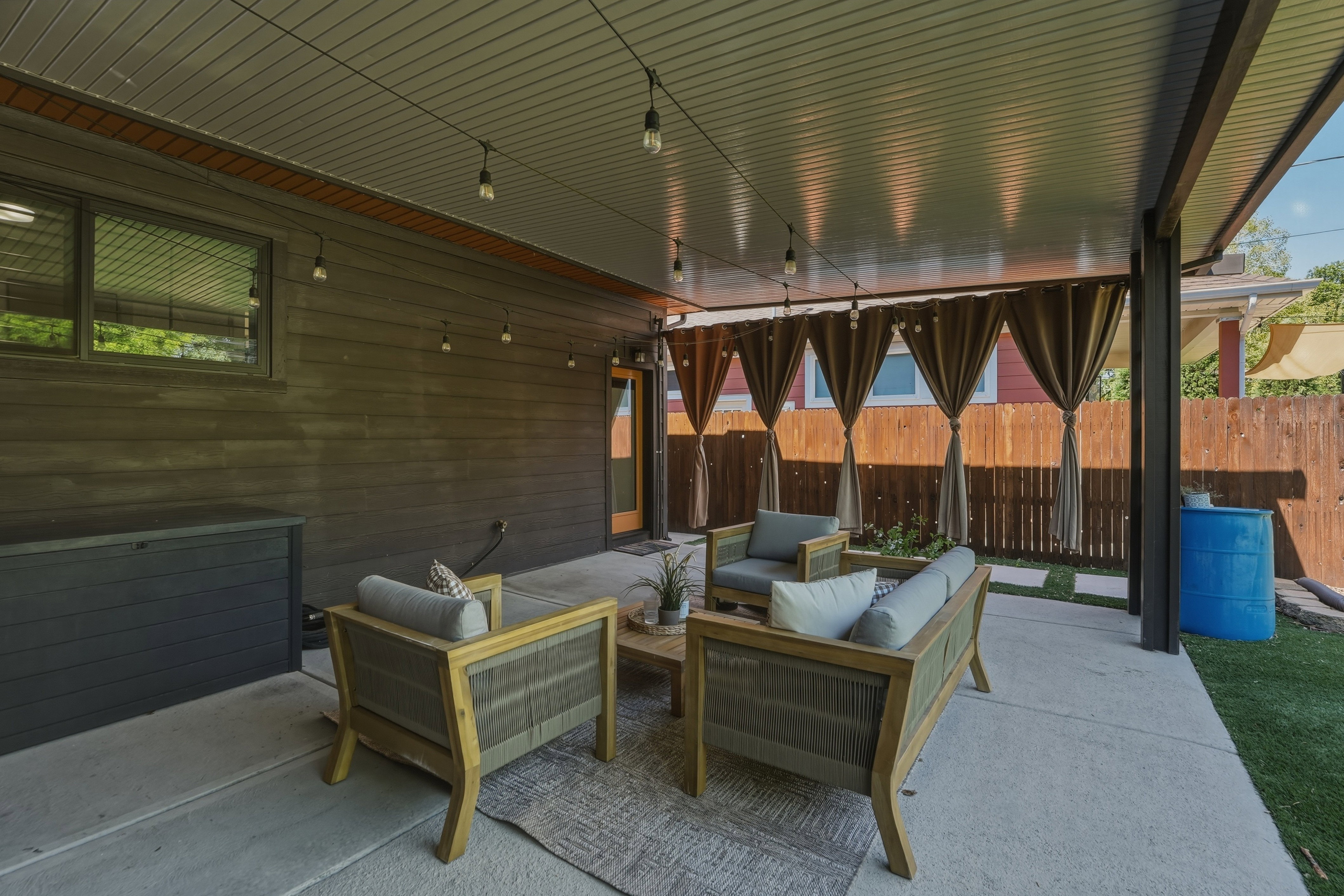 Covered patio featuring a concrete slab, string lighting, privacy curtains, and a wooden fence