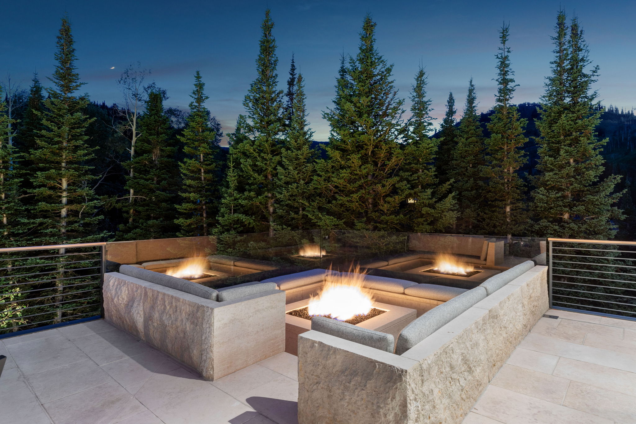 Stone patio with multiple fire pits, integrated stone seating, and a modern metal railing