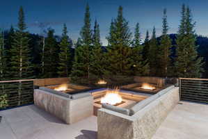 Stone patio with multiple fire pits, integrated stone seating, and a modern metal railing