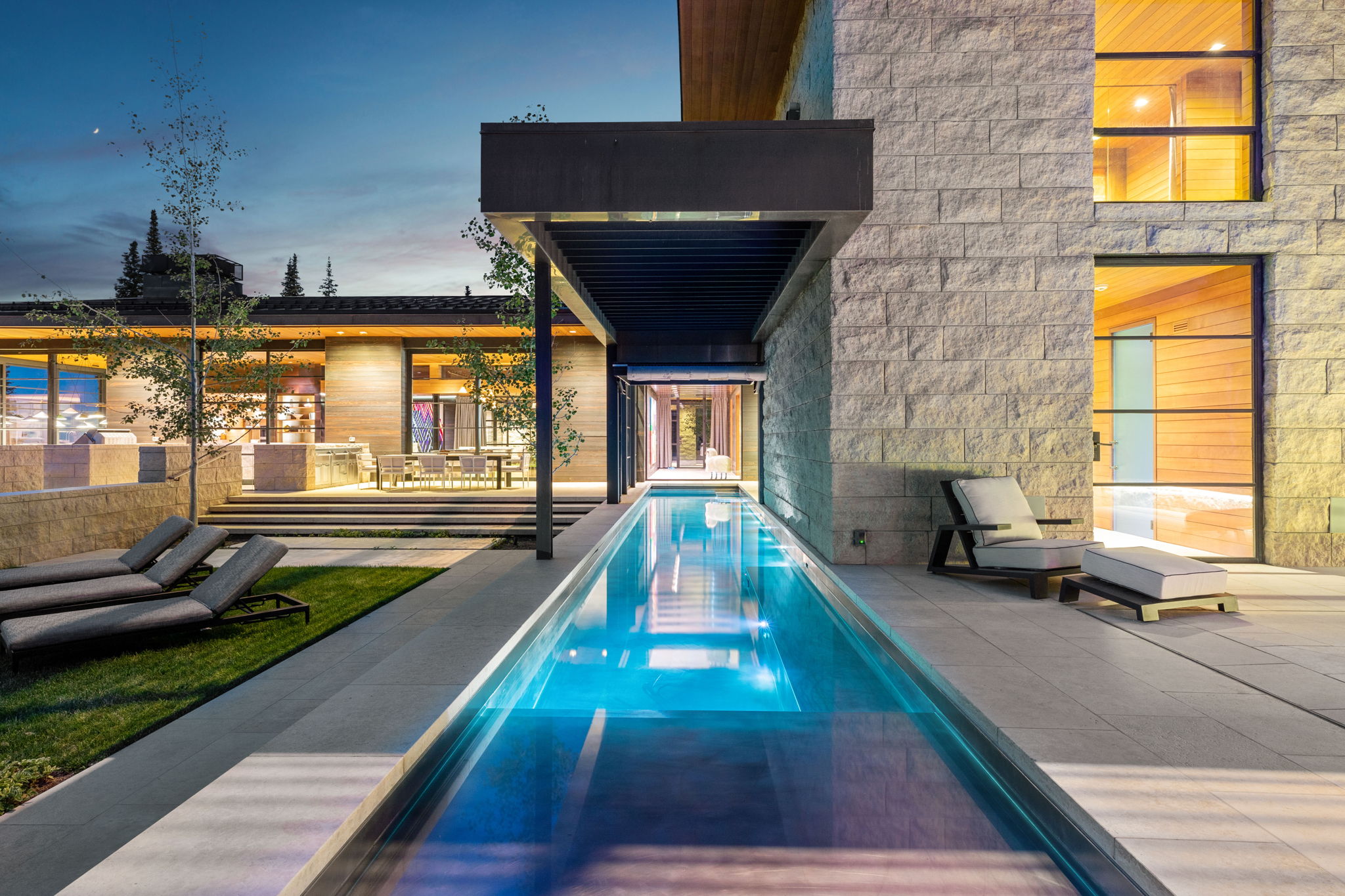Sleek linear pool with integrated lighting, surrounded by extensive patio decking and a manicured lawn