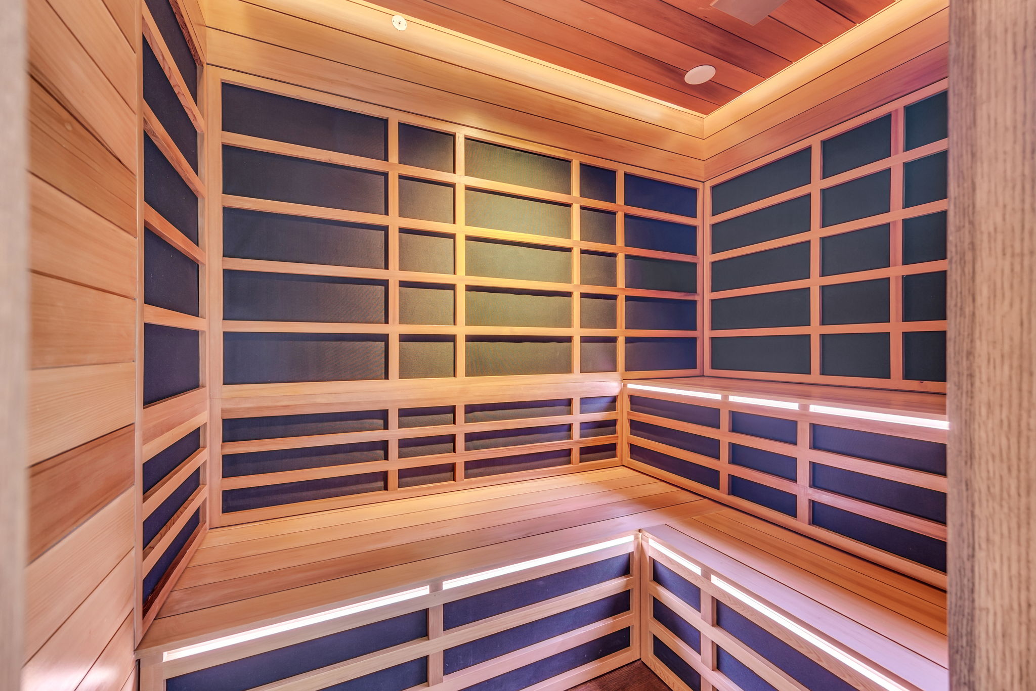 Custom-built sauna featuring wood-paneled walls and ceiling, multi-level seating, recessed lighting, and wall-mounted heating elements