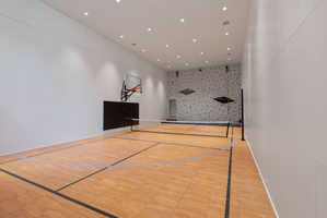 Indoor multi-sport court featuring wood-finish flooring with court markings, a basketball hoop, and a net