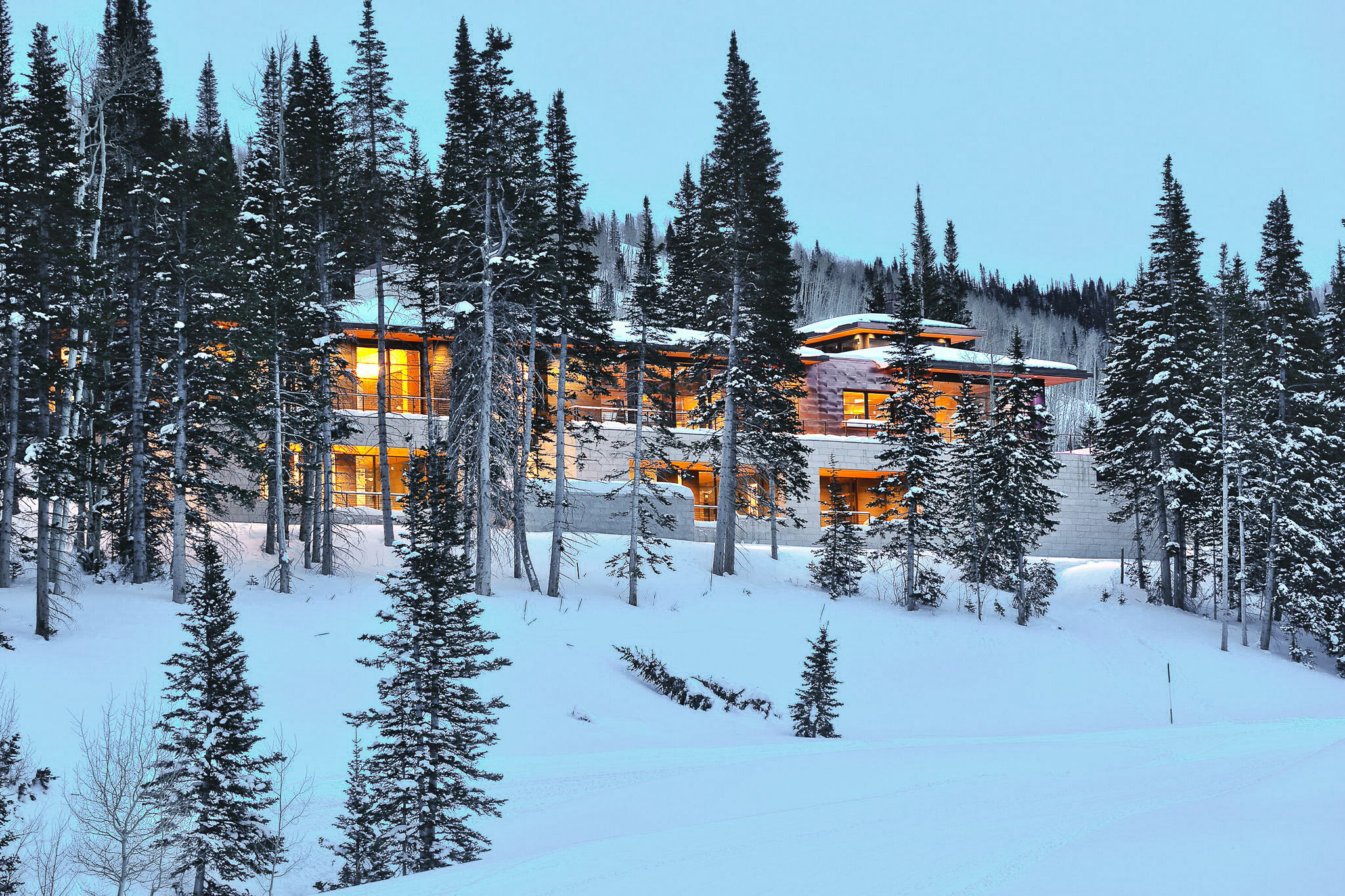 Contemporary mountain-style residence featuring extensive glazing, stacked stone exterior elements, and a multi-tiered roofline