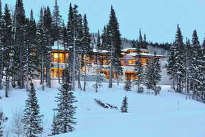 Contemporary mountain-style residence featuring extensive glazing, stacked stone exterior elements, and a multi-tiered roofline