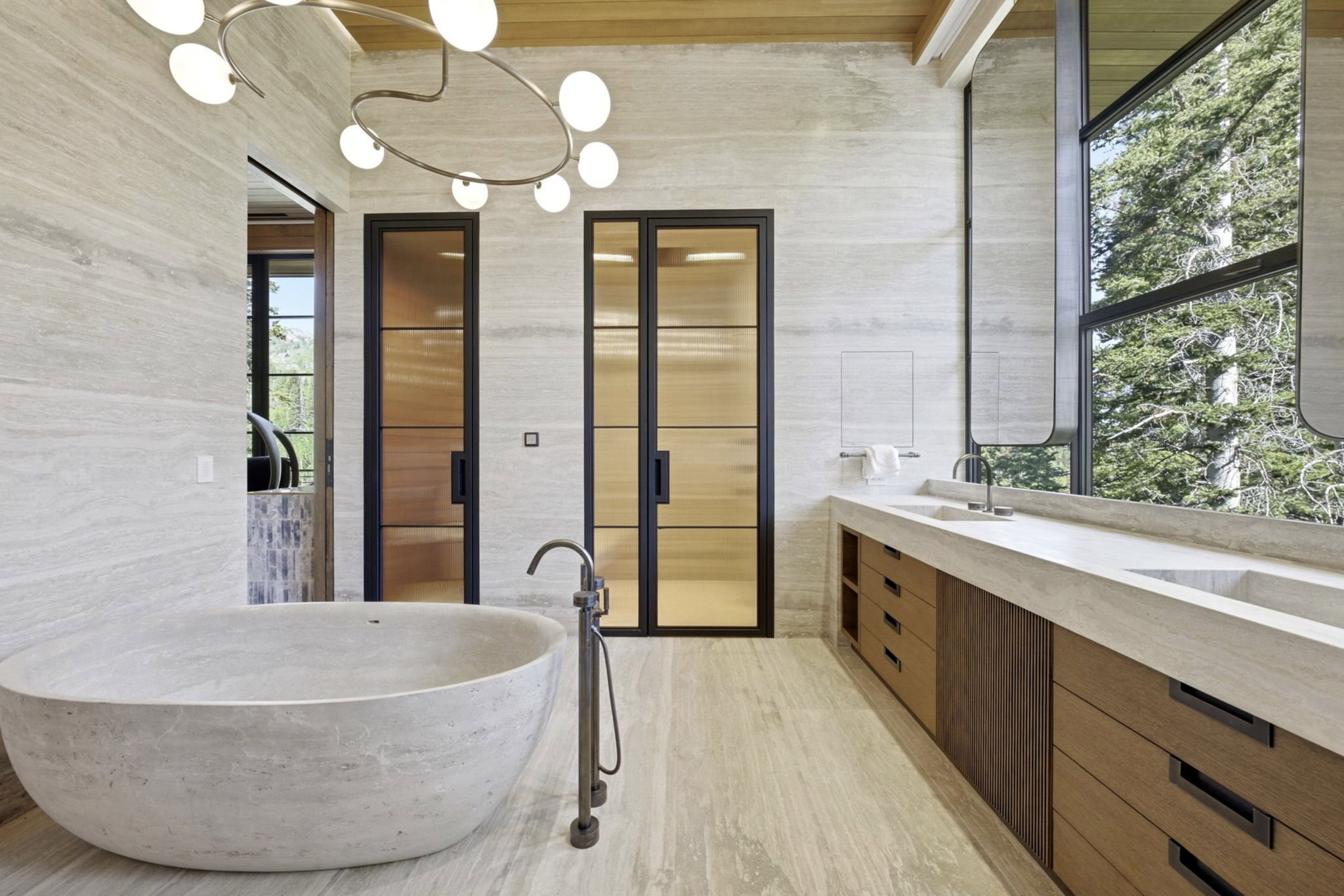 Freestanding soaking tub with a floor-mounted faucet, complemented by a long vanity with integrated sinks, wood-finish cabinetry, and a large window