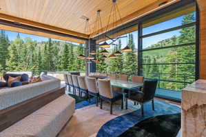 Expansive dining area featuring floor-to-ceiling windows, a wood-paneled ceiling, and a linear multi-pendant light fixture