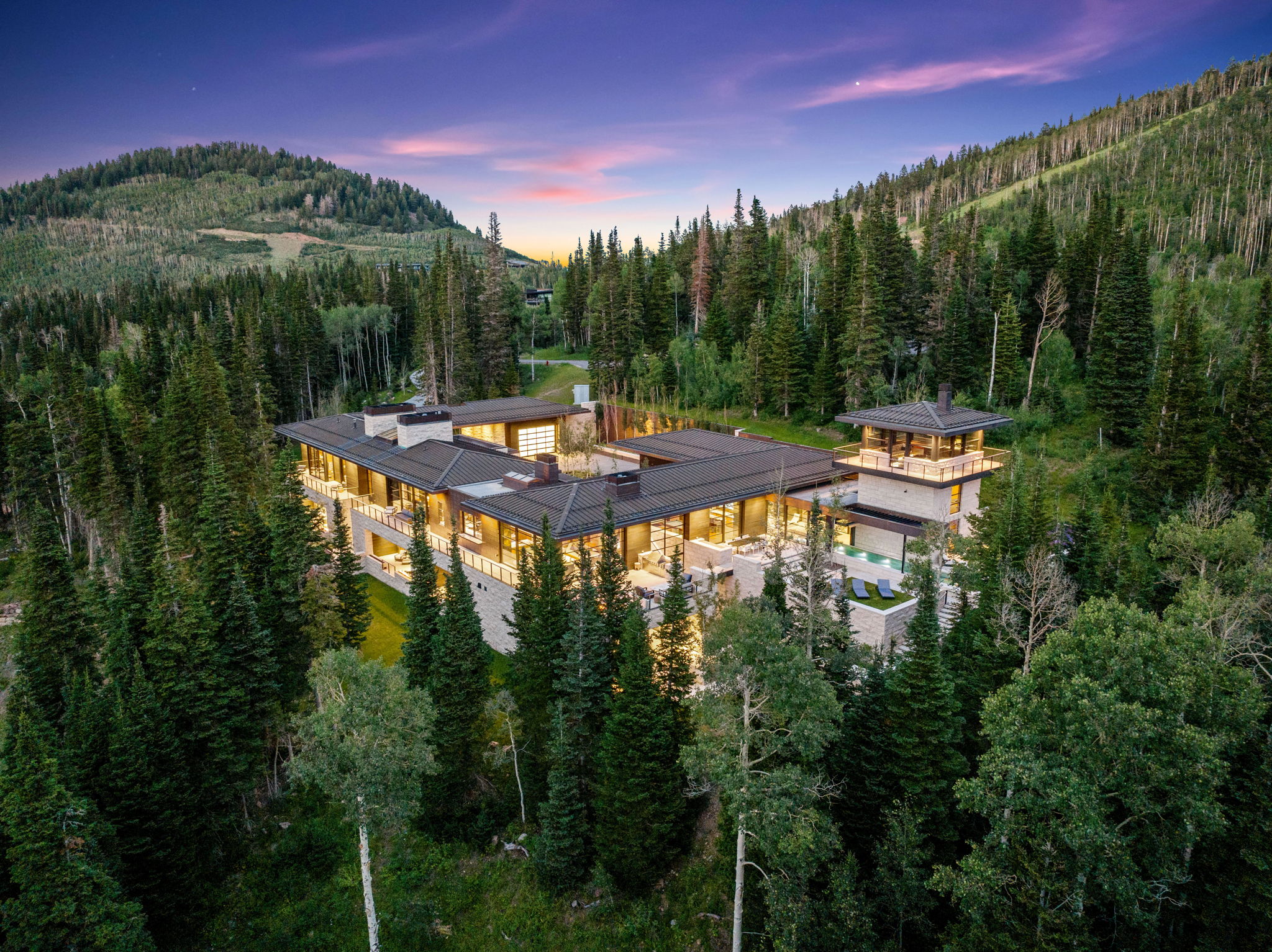 Grand mountain estate featuring extensive glass walls, multiple balconies, a distinct observation tower, and an integrated outdoor pool
