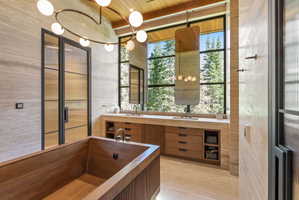 Wood-finish soaking tub with floor-mounted fixtures, set against stone-tiled walls