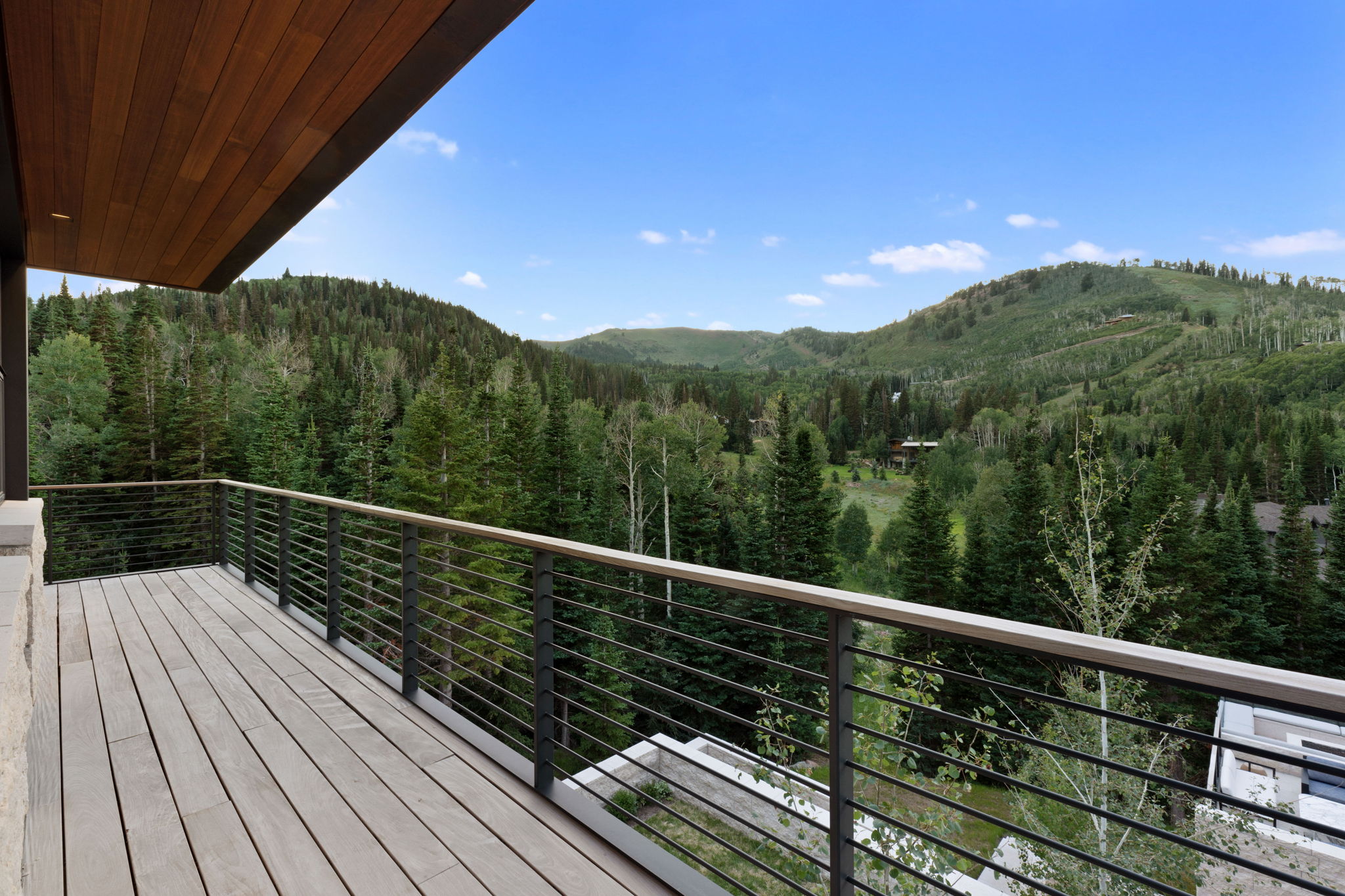 Expansive outdoor deck featuring wood-finish flooring, cable railing, wood-paneled ceiling, and broad mountain scenery