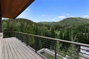 Expansive outdoor deck featuring wood-finish flooring, cable railing, wood-paneled ceiling, and broad mountain scenery