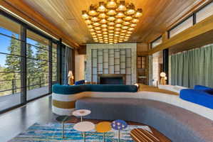 Expansive living space featuring a wood-panel ceiling, full-height windows, and a stone-clad fireplace