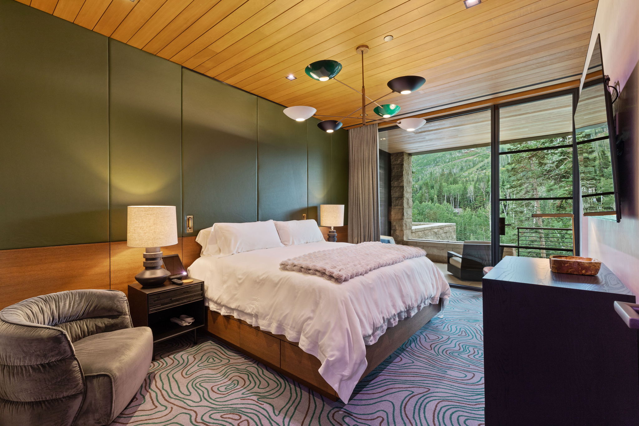 Bedroom featuring a wood-panel ceiling, full-height glass doors, and expansive forest scenery