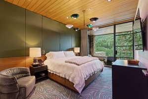 Bedroom featuring a wood-panel ceiling, full-height glass doors, and expansive forest scenery
