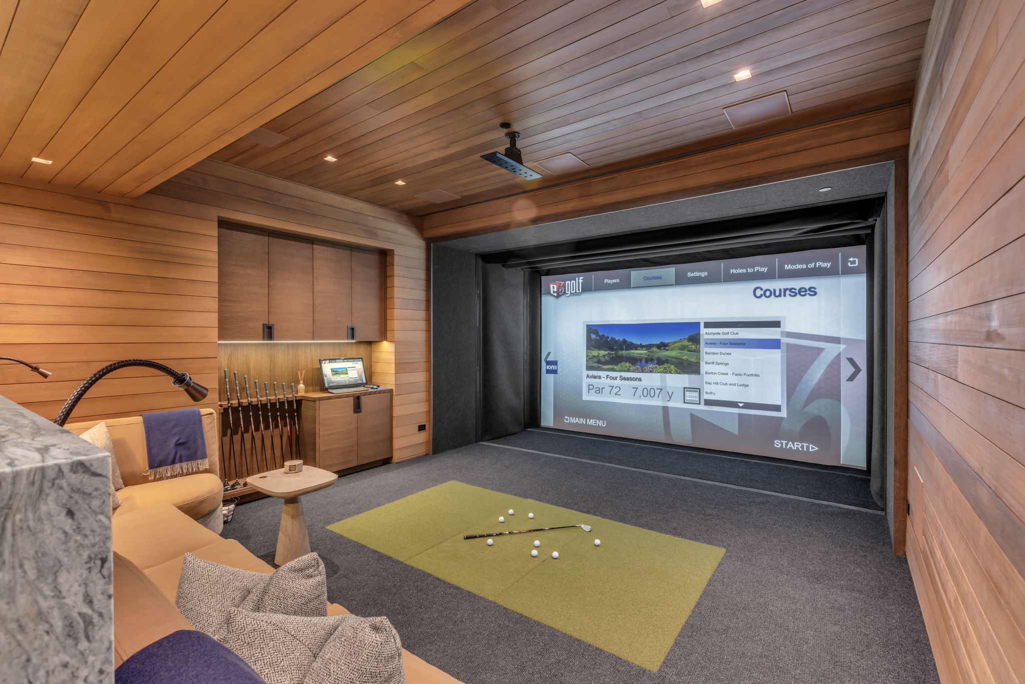 Dedicated entertainment space featuring a large projection screen, wood-paneled walls and ceiling, recessed lighting, built-in cabinetry with integrated lighting, and dark gray carpeting