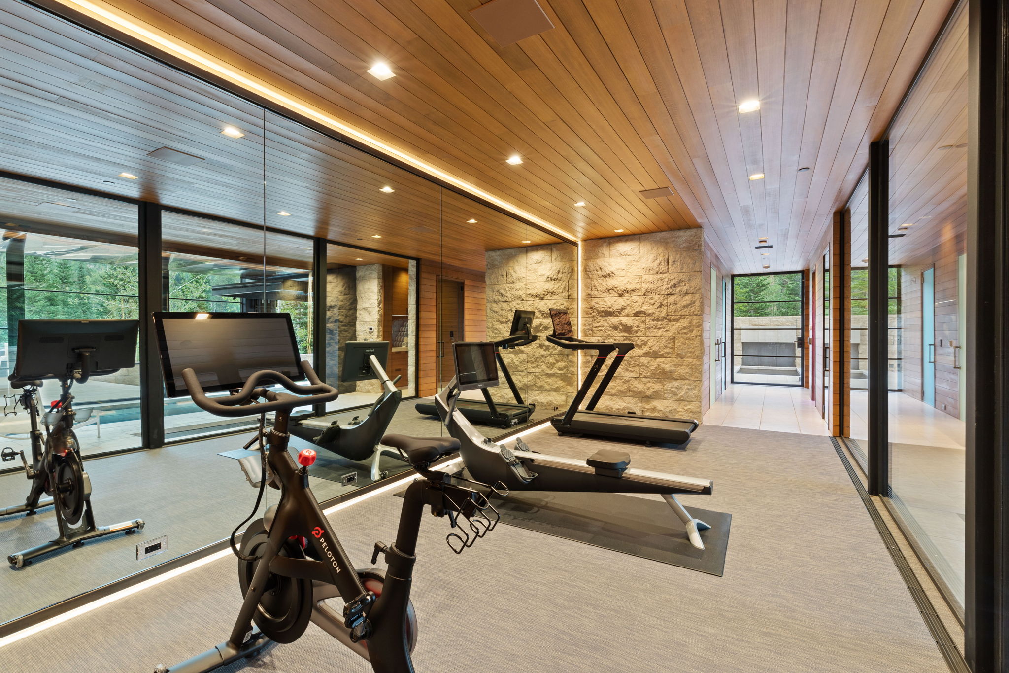 Dedicated fitness area featuring wood-finish ceiling, stone accent walls, recessed lighting, and full-length mirrored walls