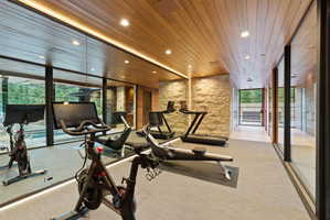 Dedicated fitness area featuring wood-finish ceiling, stone accent walls, recessed lighting, and full-length mirrored walls