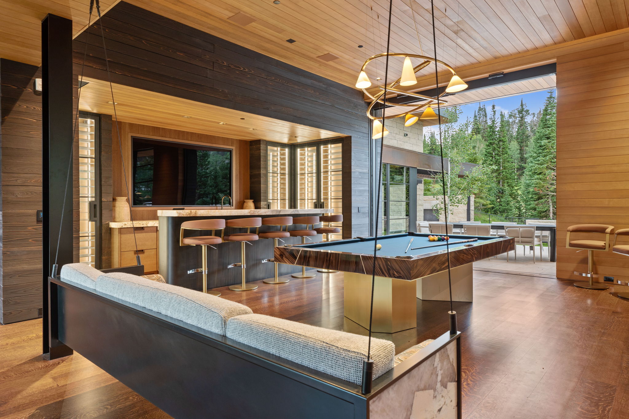 Expansive entertainment space featuring wood-finish flooring, a built-in wet bar with stone countertop, a billiards table, and a suspended swing seat