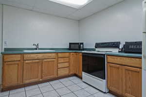 Kitchenette featuring wood-finish cabinetry, a white drop-in sink with a chrome faucet, and a black and white electric range