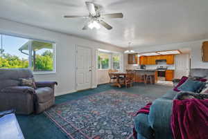 Open-concept living area featuring a ceiling fan, broad windows, and a carpeted floor