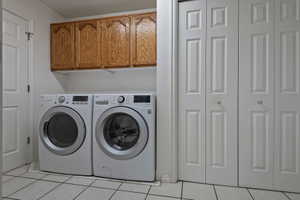 Laundry area featuring overhead wood-finish cabinetry, tile flooring, and bi-fold doors
