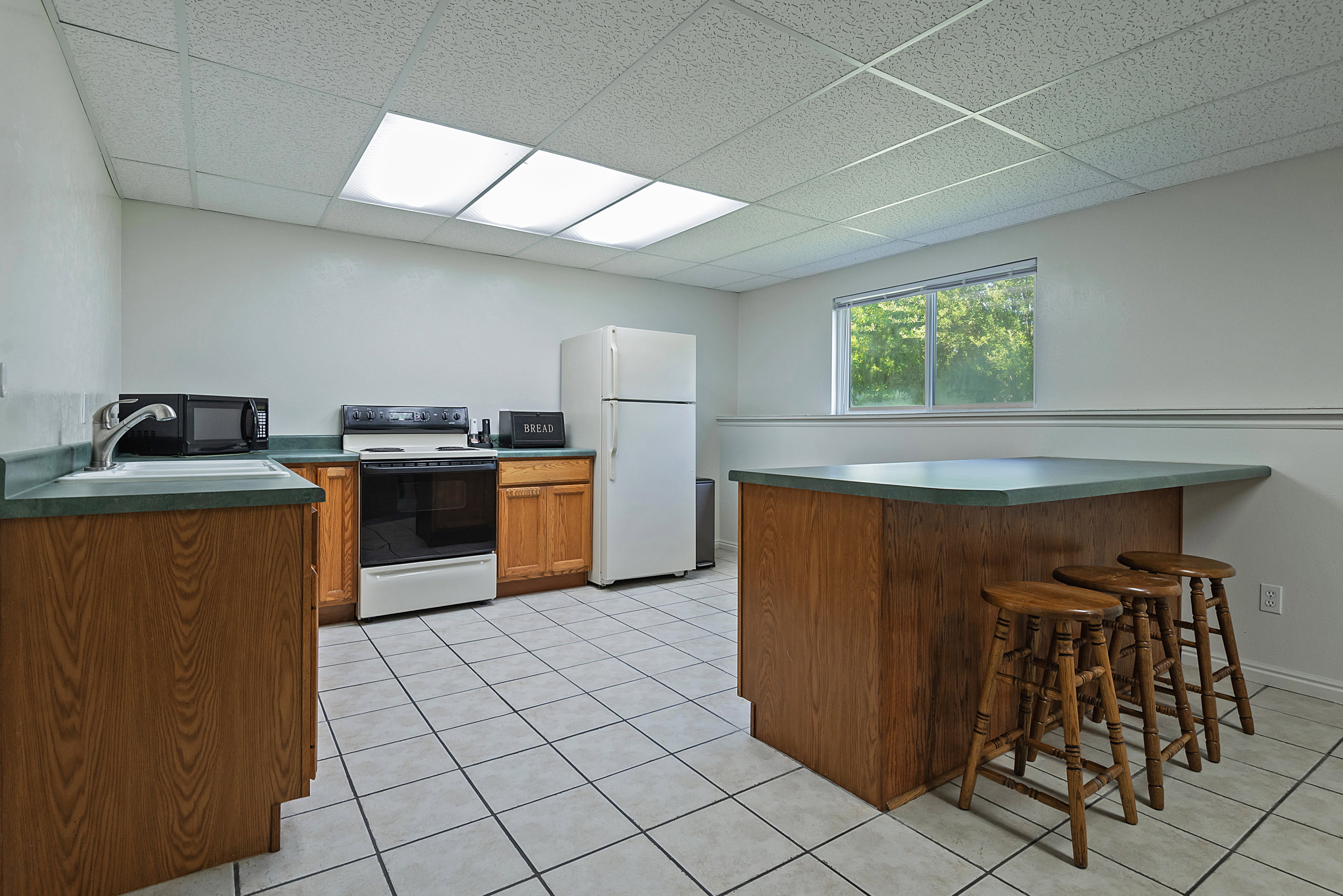 Kitchen space featuring wood-finish cabinetry, light-toned tile flooring, and a drop ceiling with recessed lighting