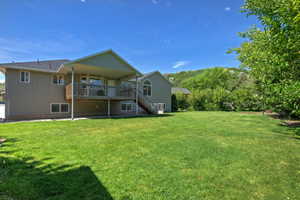 Expansive green lawn with a covered deck, wood handrails, and exterior stairs