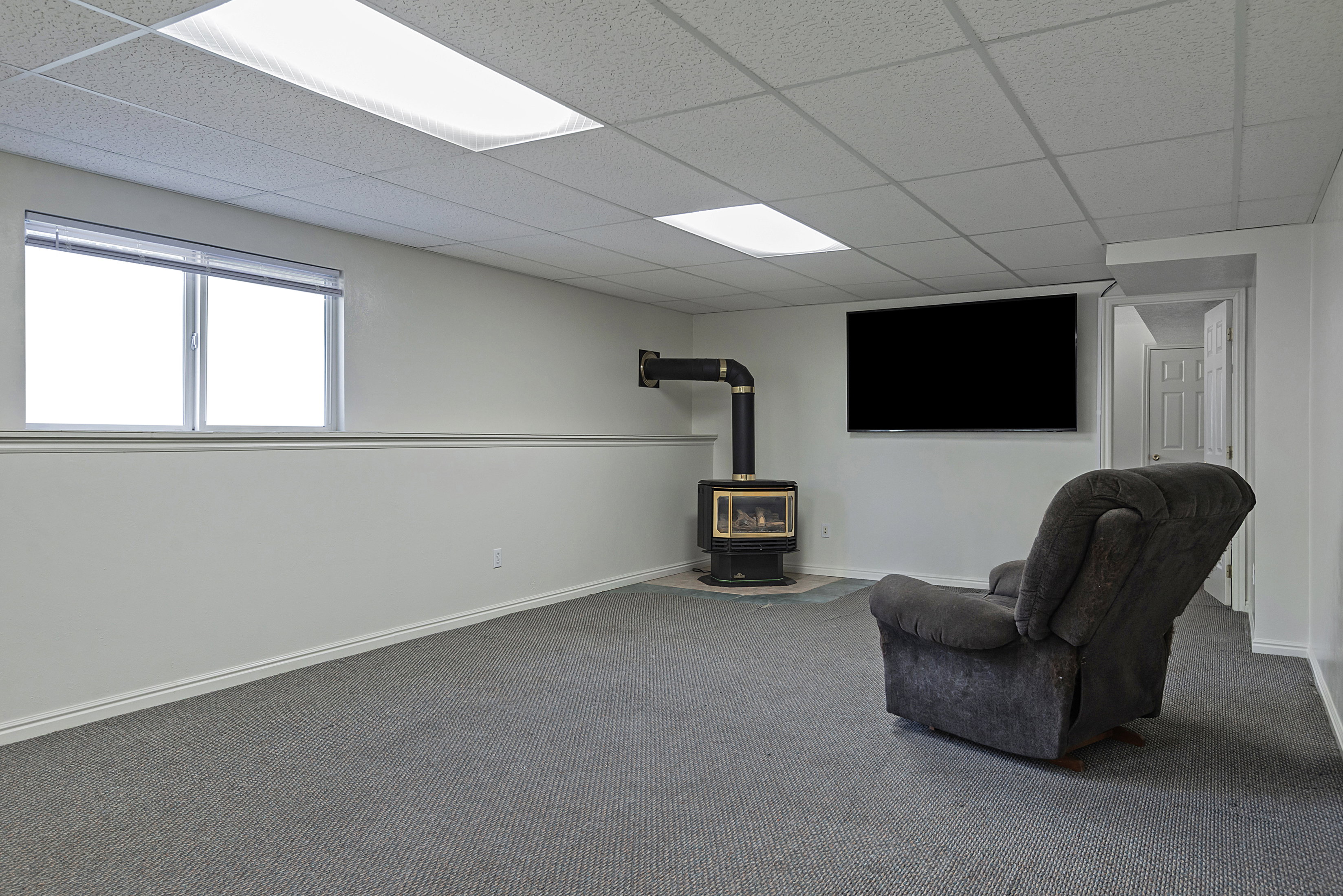 Carpeted entertainment area featuring a mounted television and a built-in wood-burning stove with a black pipe vent