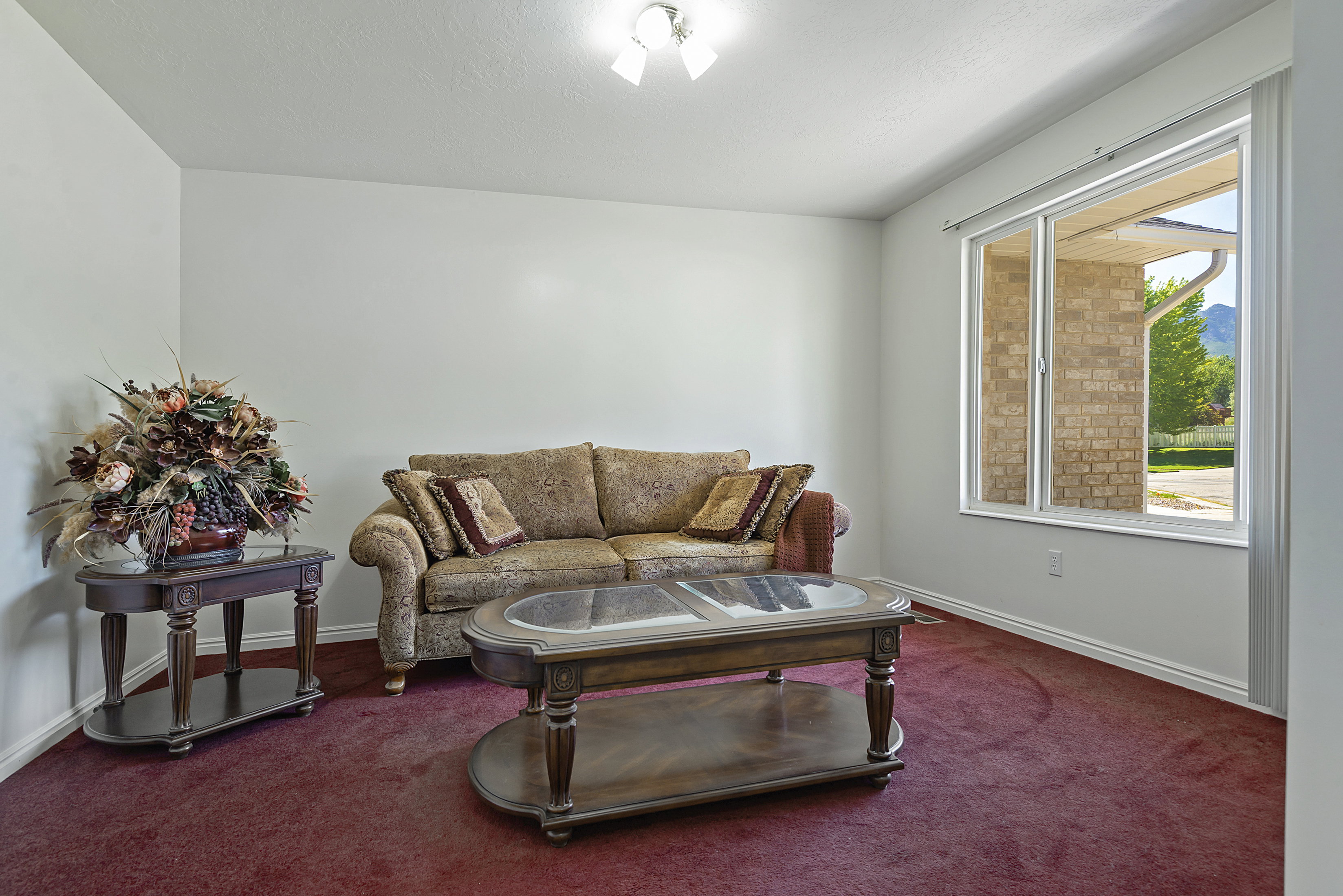 Spacious living area featuring light-colored walls, red carpet flooring, a large window, and white trim
