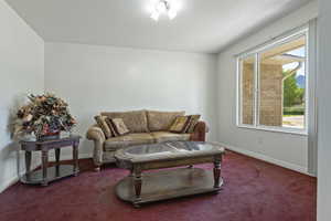 Spacious living area featuring light-colored walls, red carpet flooring, a large window, and white trim