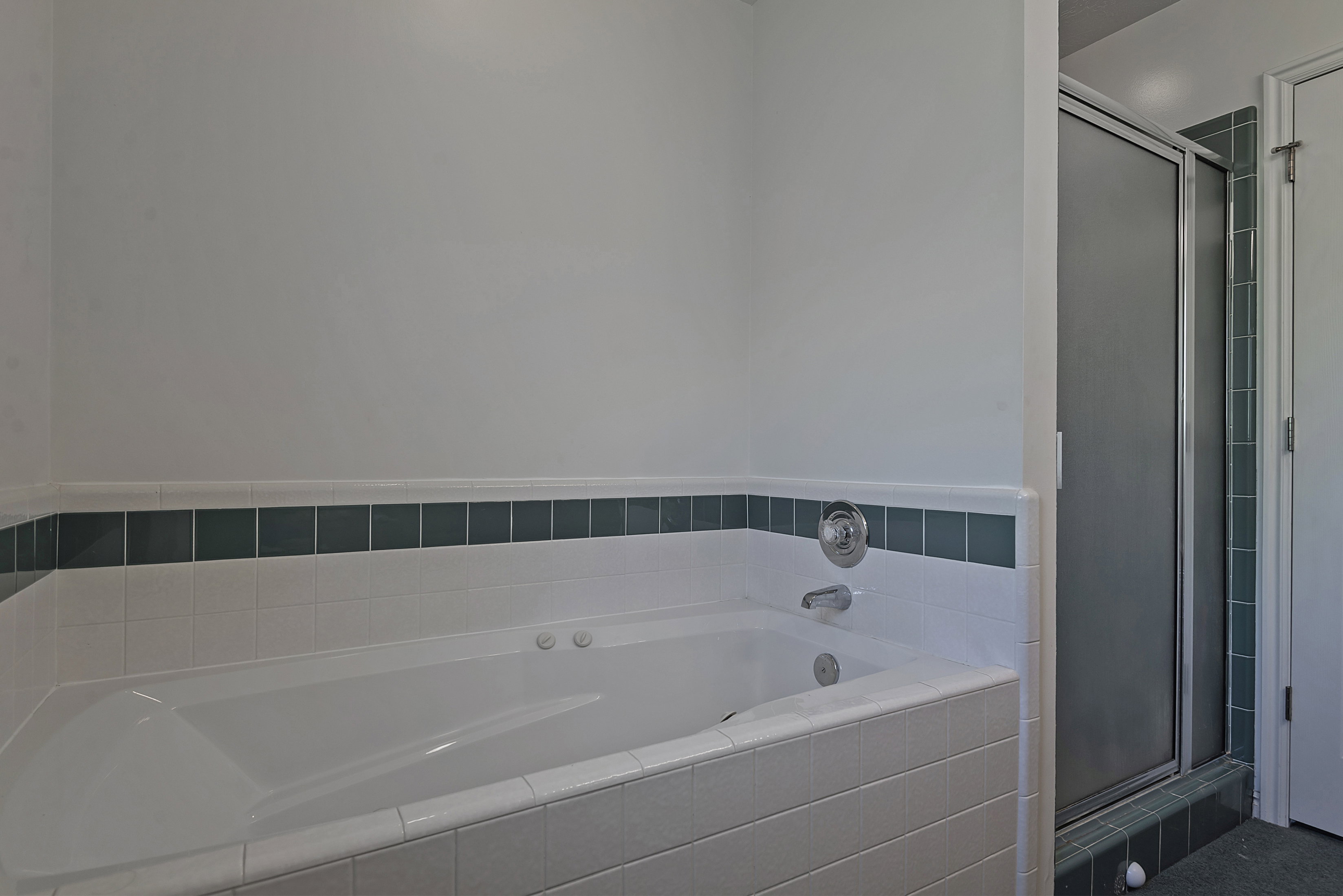 White drop-in jetted bathtub with chrome fixtures and white tile surround