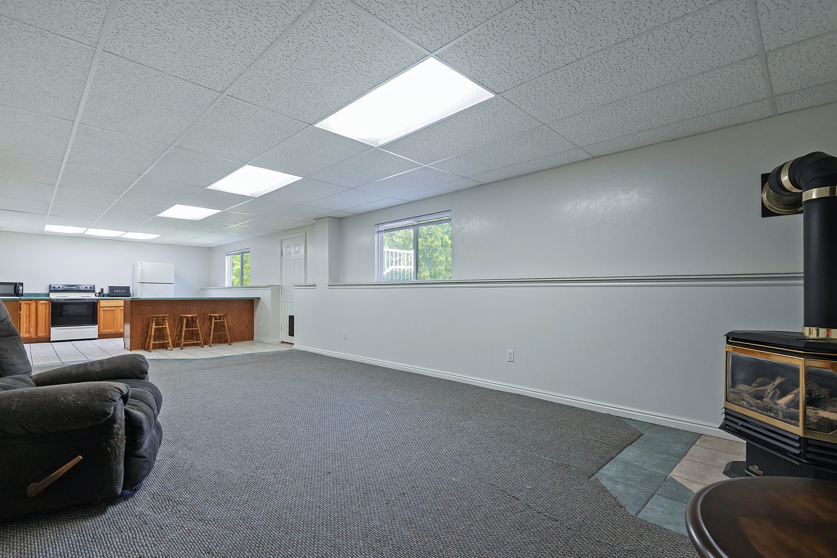 Spacious lower level featuring a modern stove fireplace with a tile hearth, a wood-finish bar, recessed lighting, wood-finish cabinetry, and white appliances