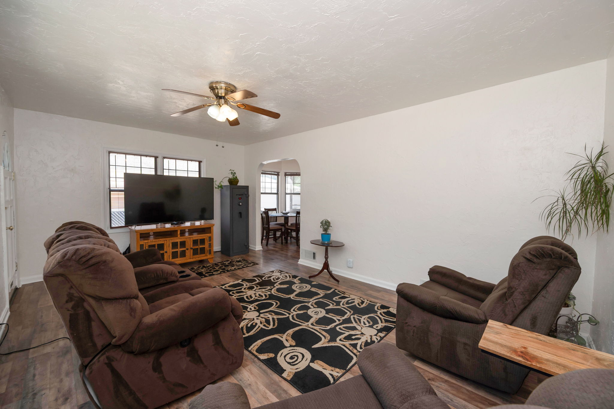 Living area featuring wood-finish flooring, a ceiling fan with integrated lighting, and multiple windows