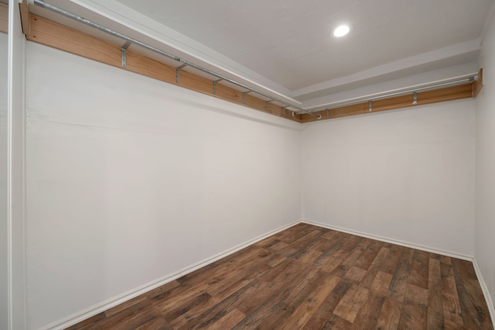 Spacious walk-in closet featuring wood-finish flooring, white walls, and built-in wood shelving with metal hanging rods