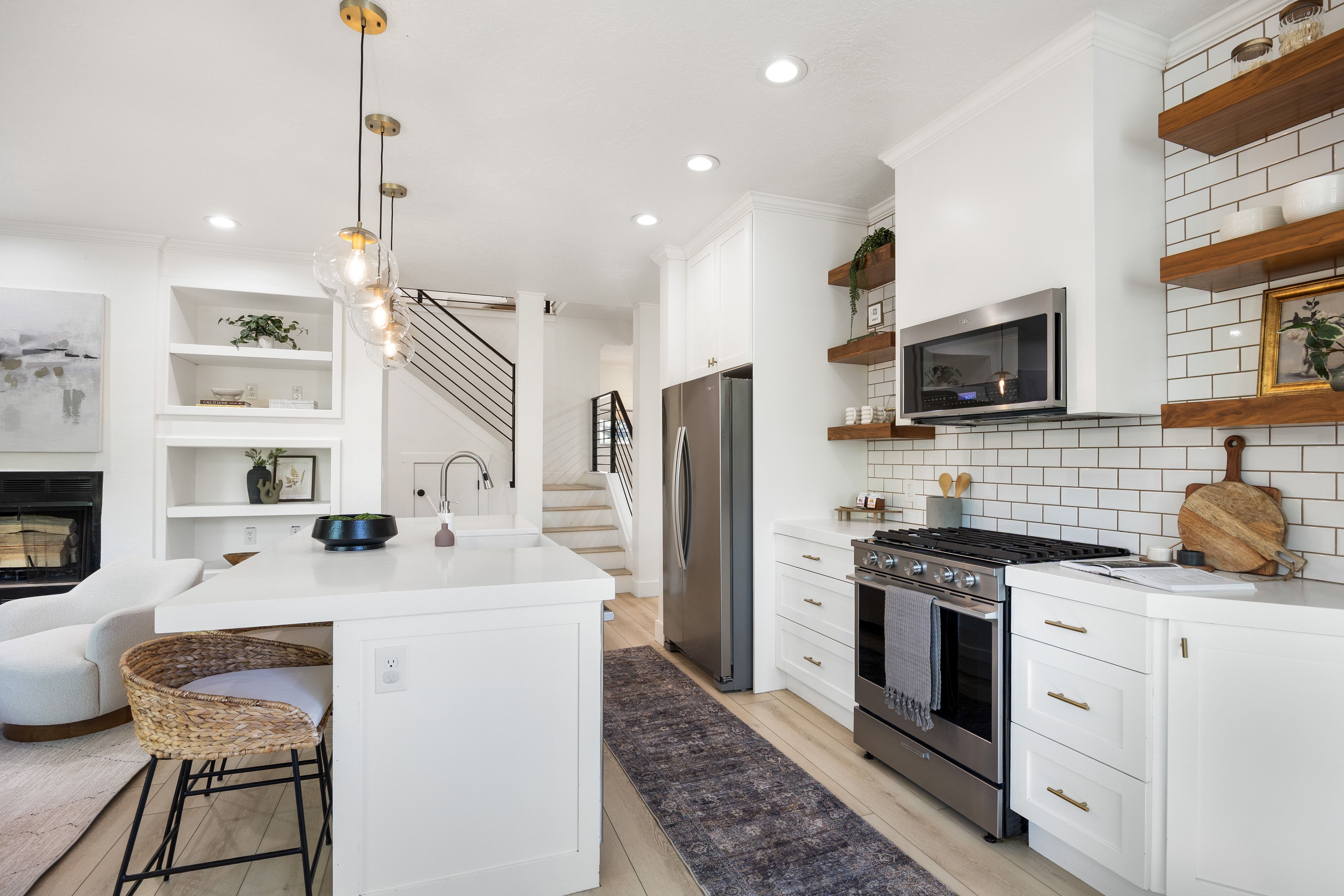 Open-concept kitchen with a large island featuring a white countertop and seating, stainless steel appliances, white subway tile backsplash, white cabinetry, and wood-finish open shelving