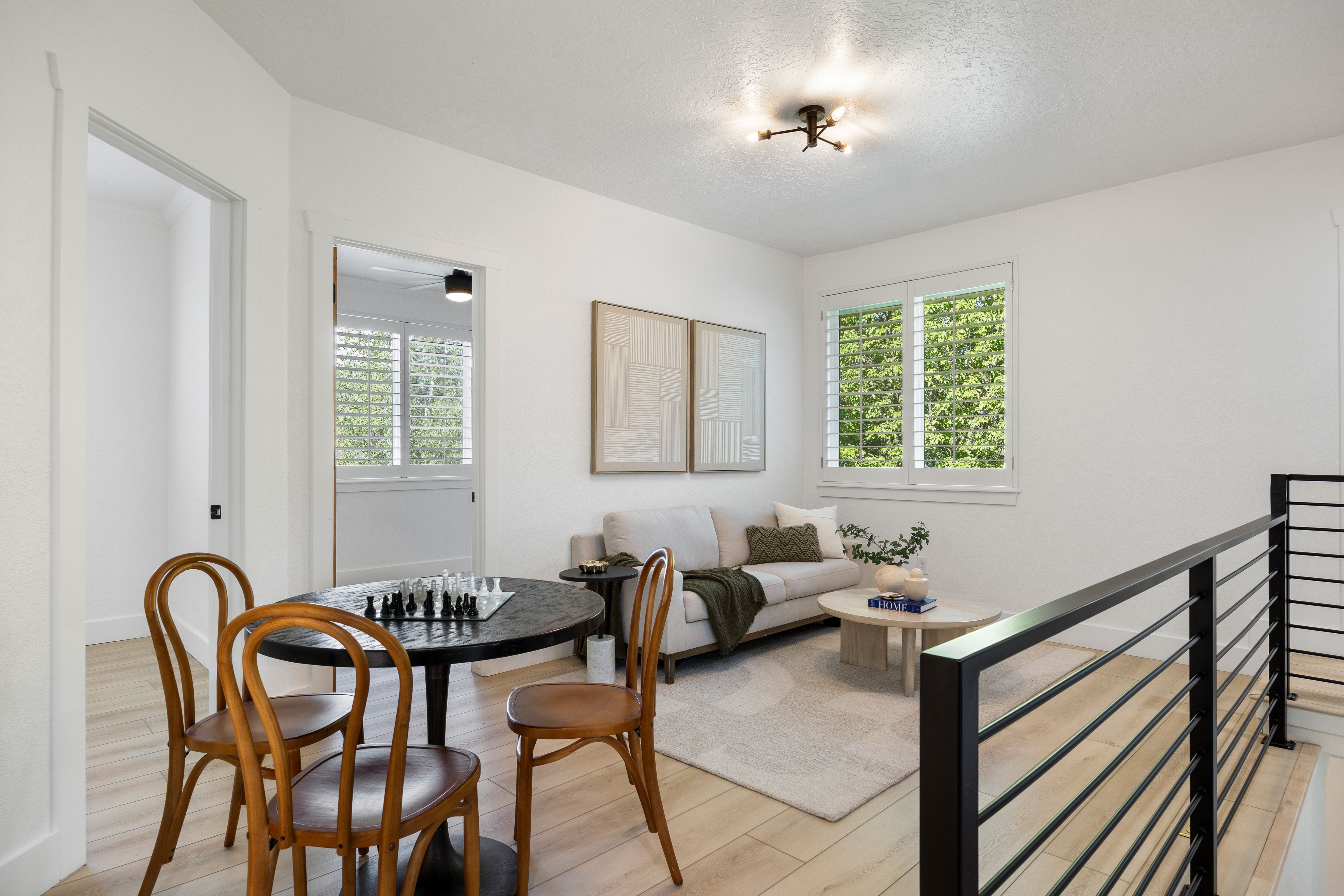 Open loft area featuring wood-finish flooring, a modern black metal railing, and white plantation shutters
