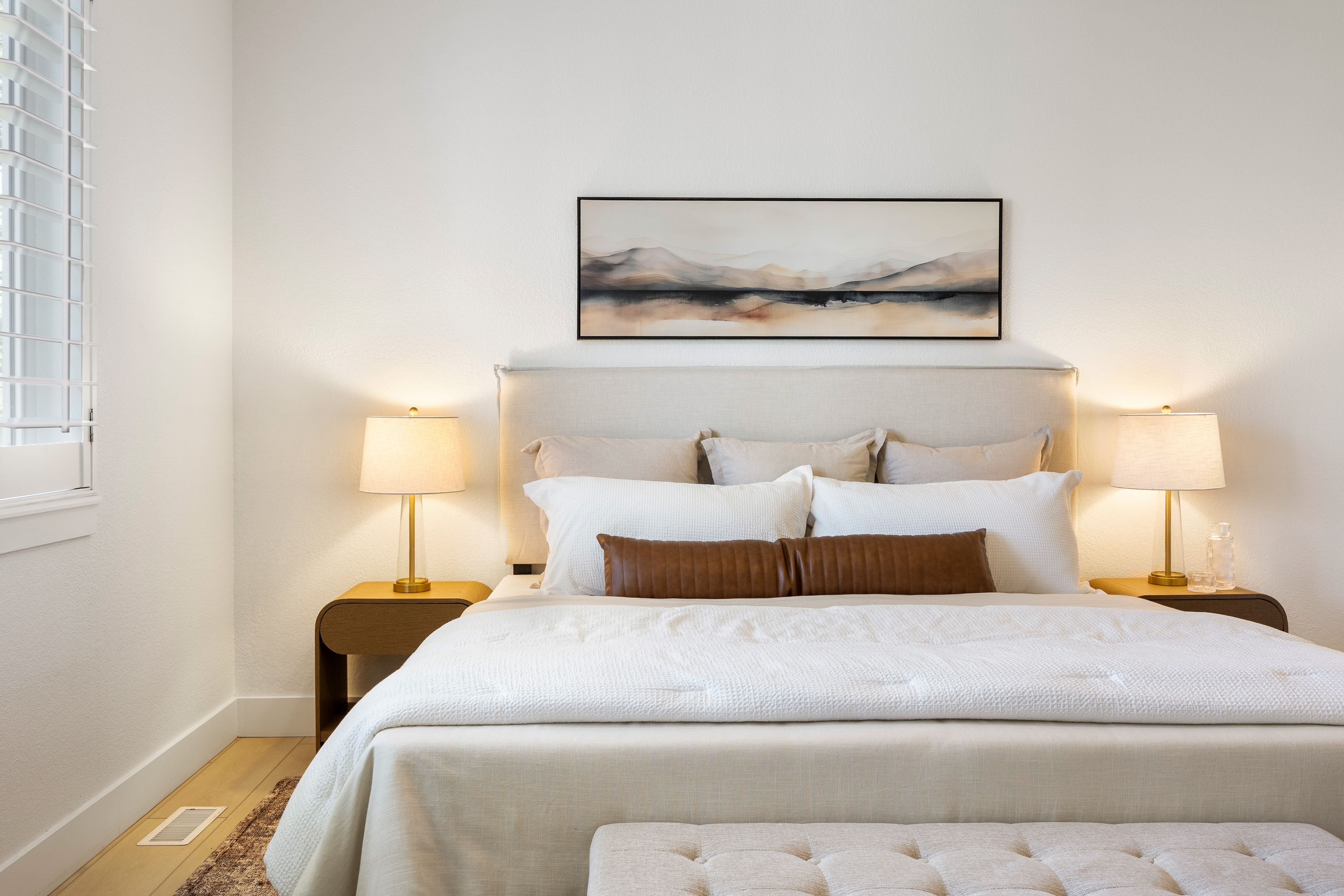 Bedroom featuring light-toned walls, wood-finish flooring, a window with louvered blinds, and a built-in upholstered headboard