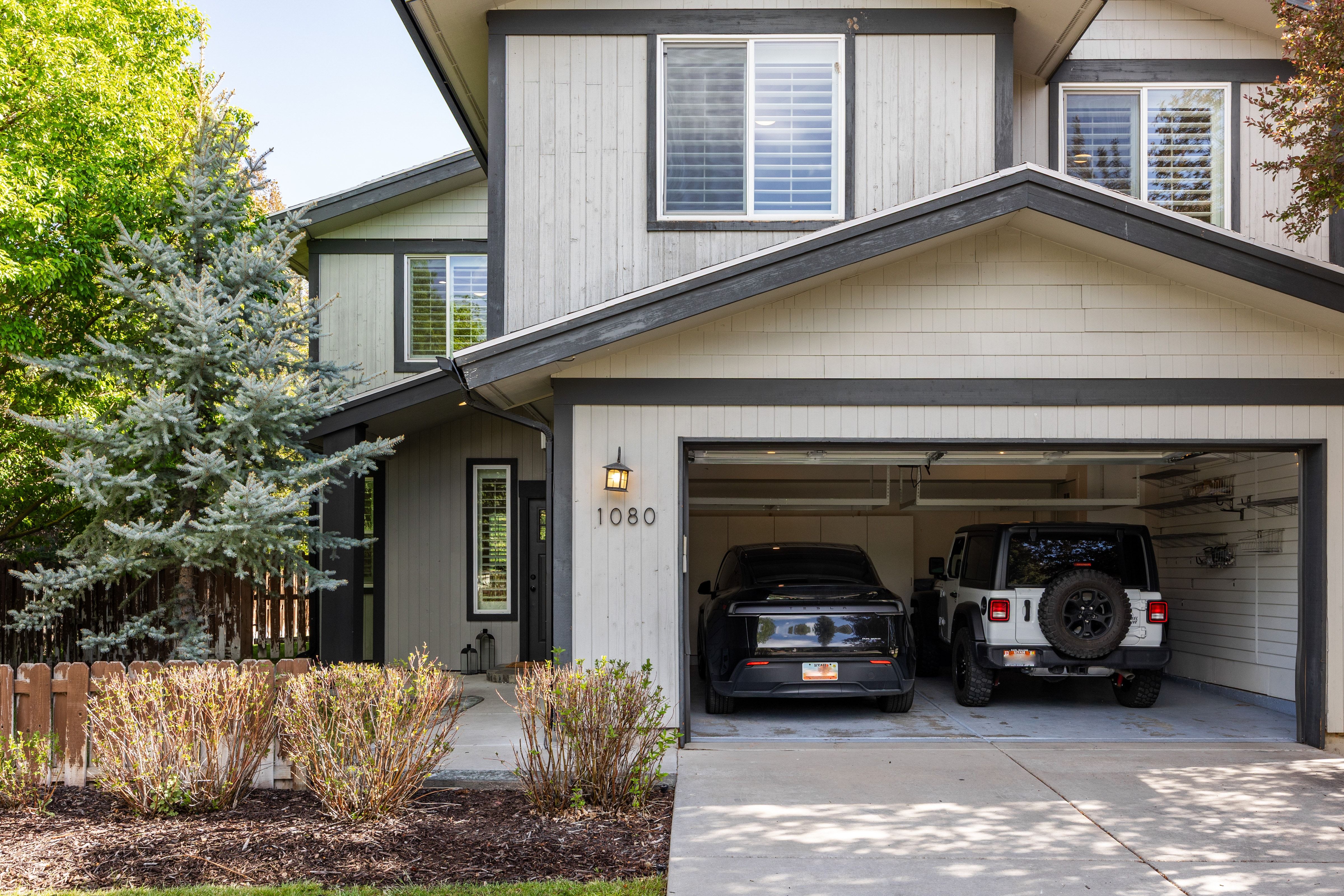 Two-story exterior featuring a two-car garage, light-toned siding, dark trim, and multiple windows with white blinds