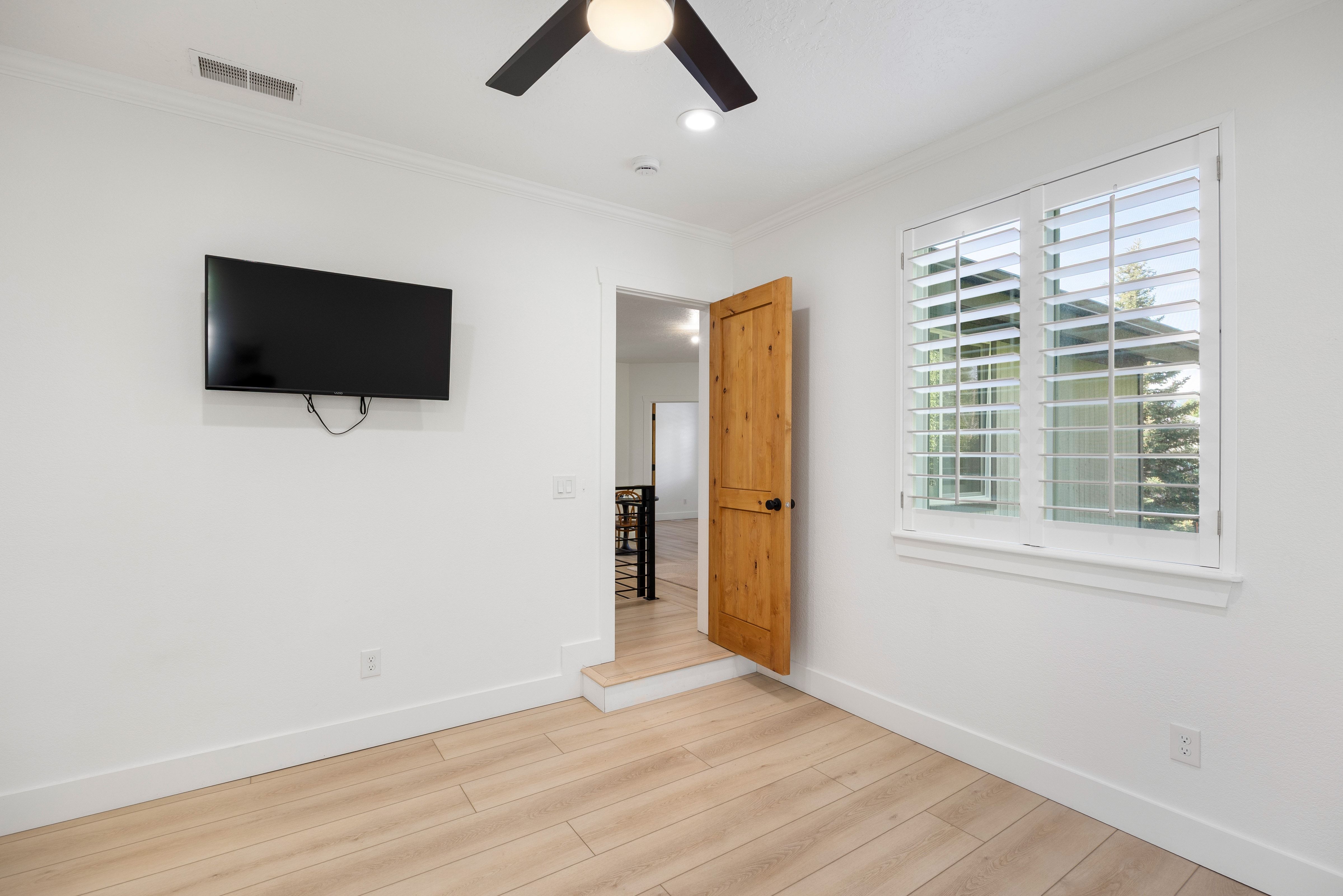 Room featuring wood-finish flooring, white walls, and a window with plantation shutters