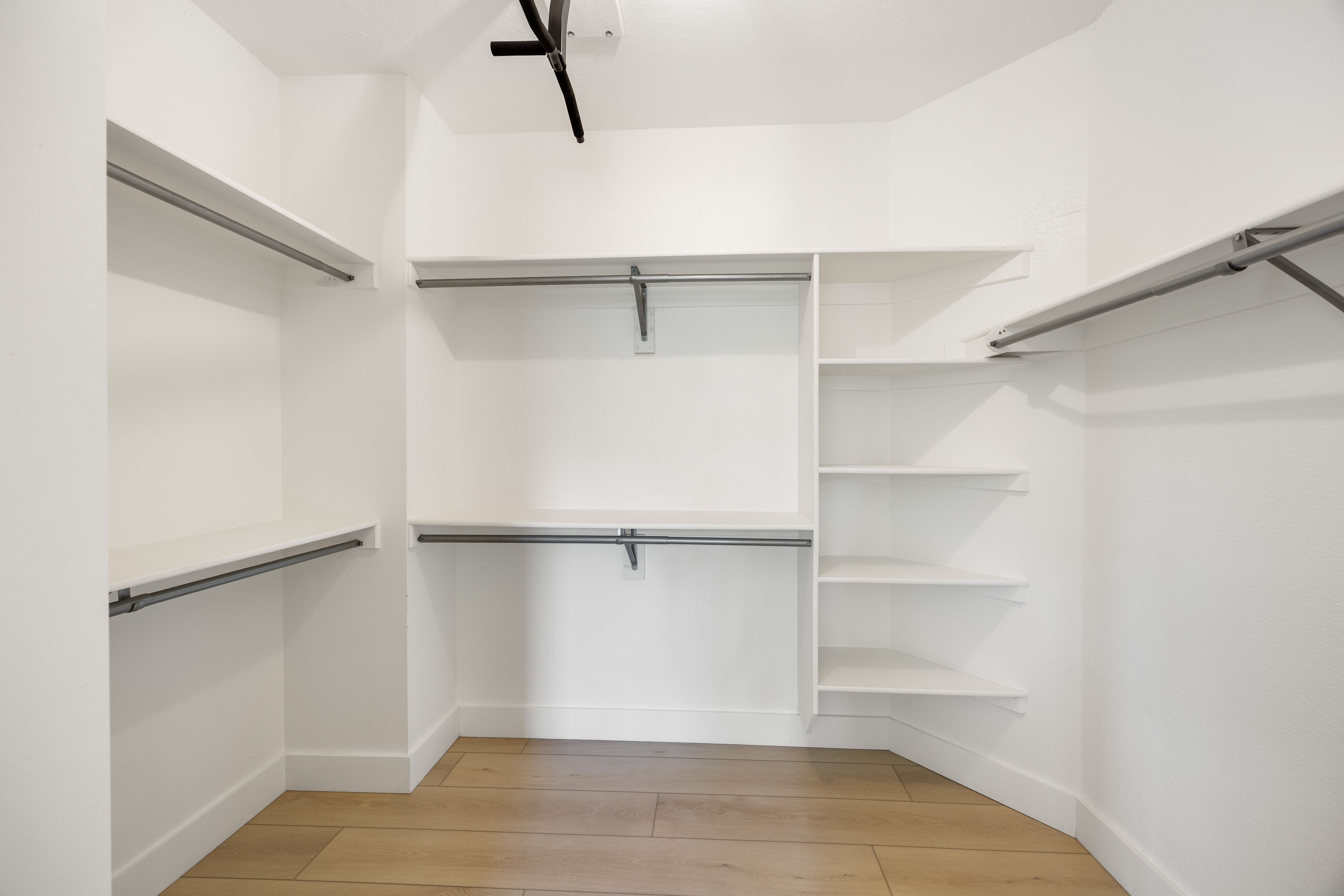 Walk-in closet featuring light wood-finish flooring, white walls, built-in shelving, and multiple clothing rods