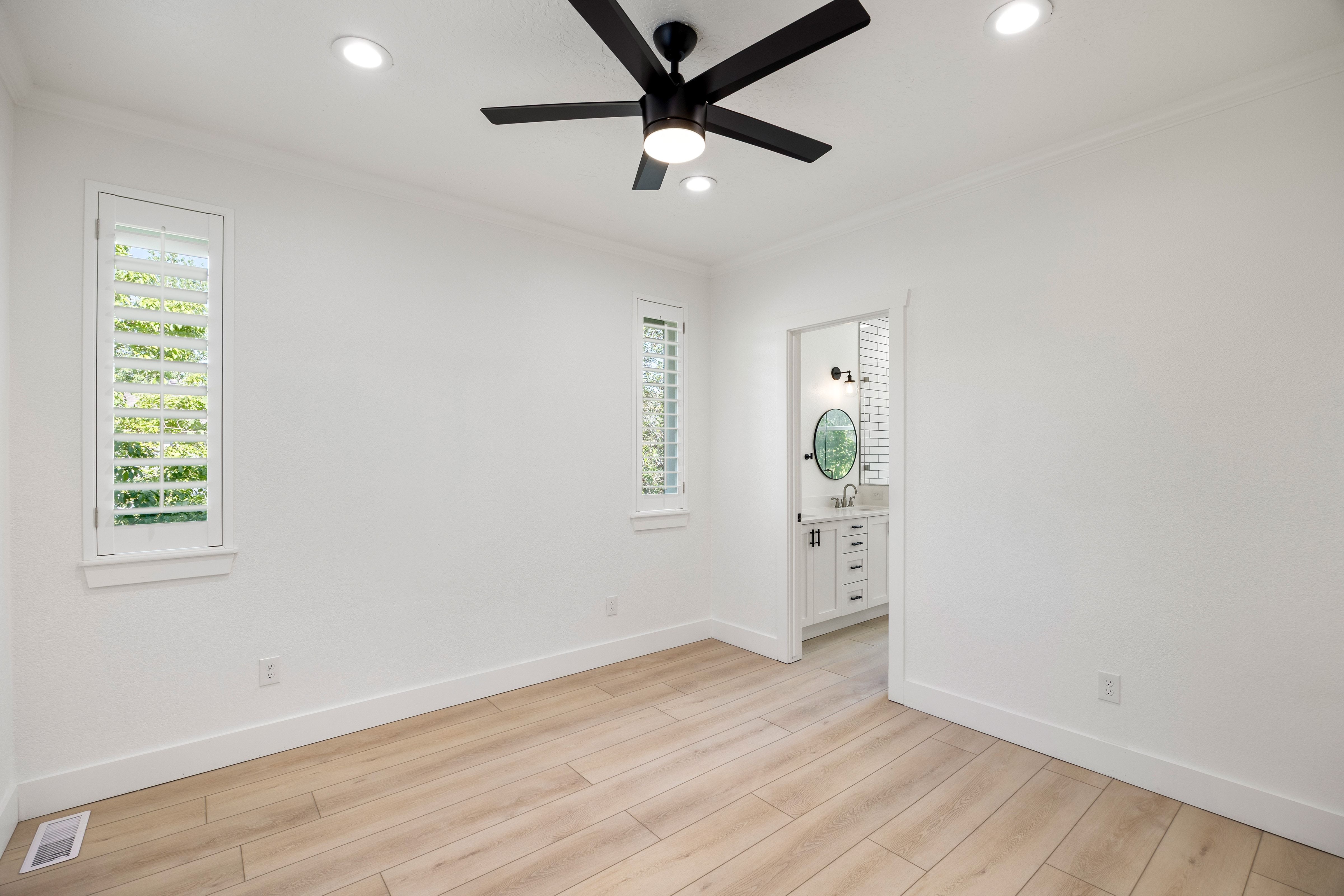 Room featuring wood-finish flooring, two vertical windows with plantation shutters, recessed lighting, and a black ceiling fan