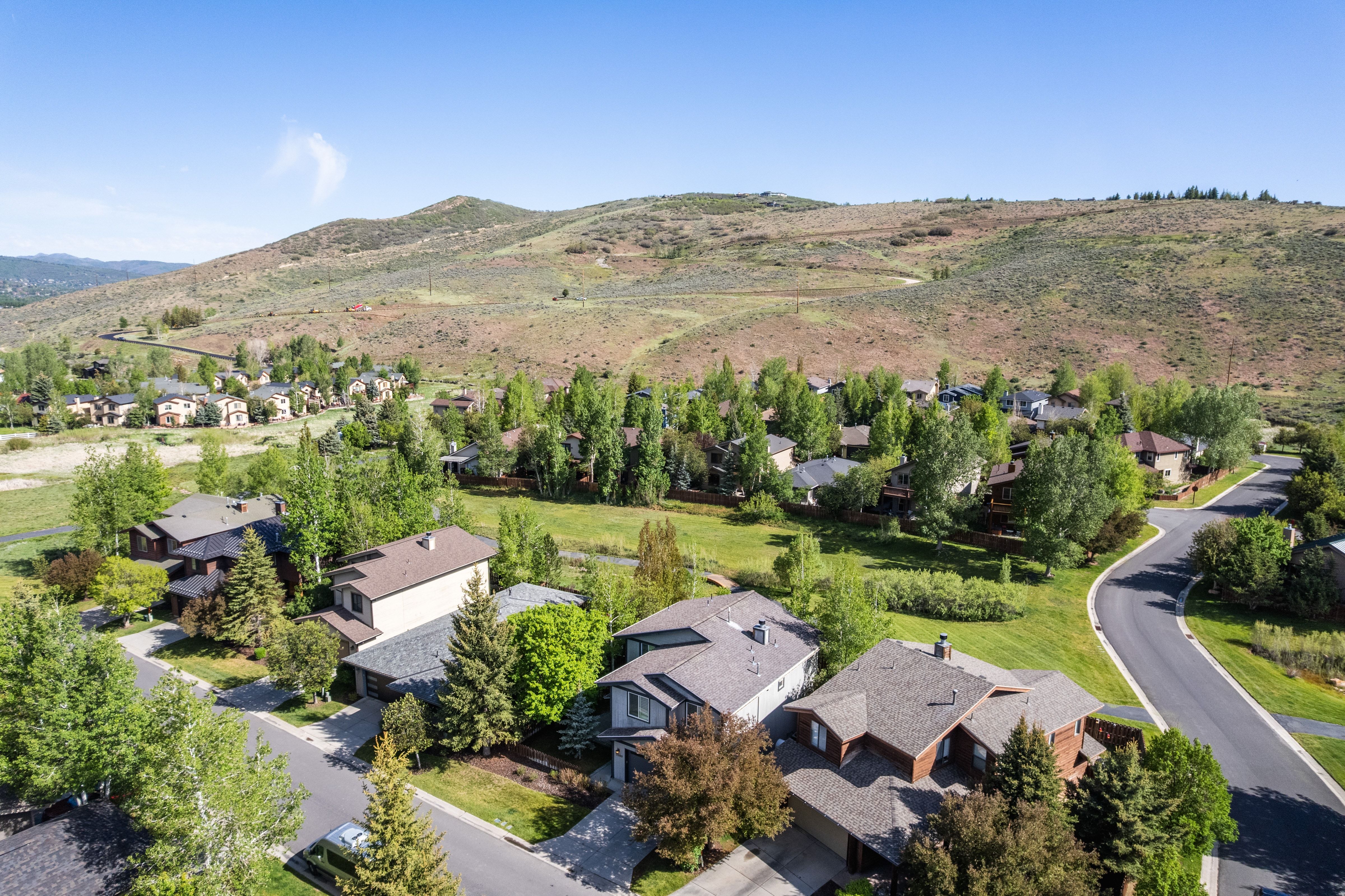 Residential neighborhood featuring a paved street, mature trees, and natural green spaces set against a backdrop of rolling hills
