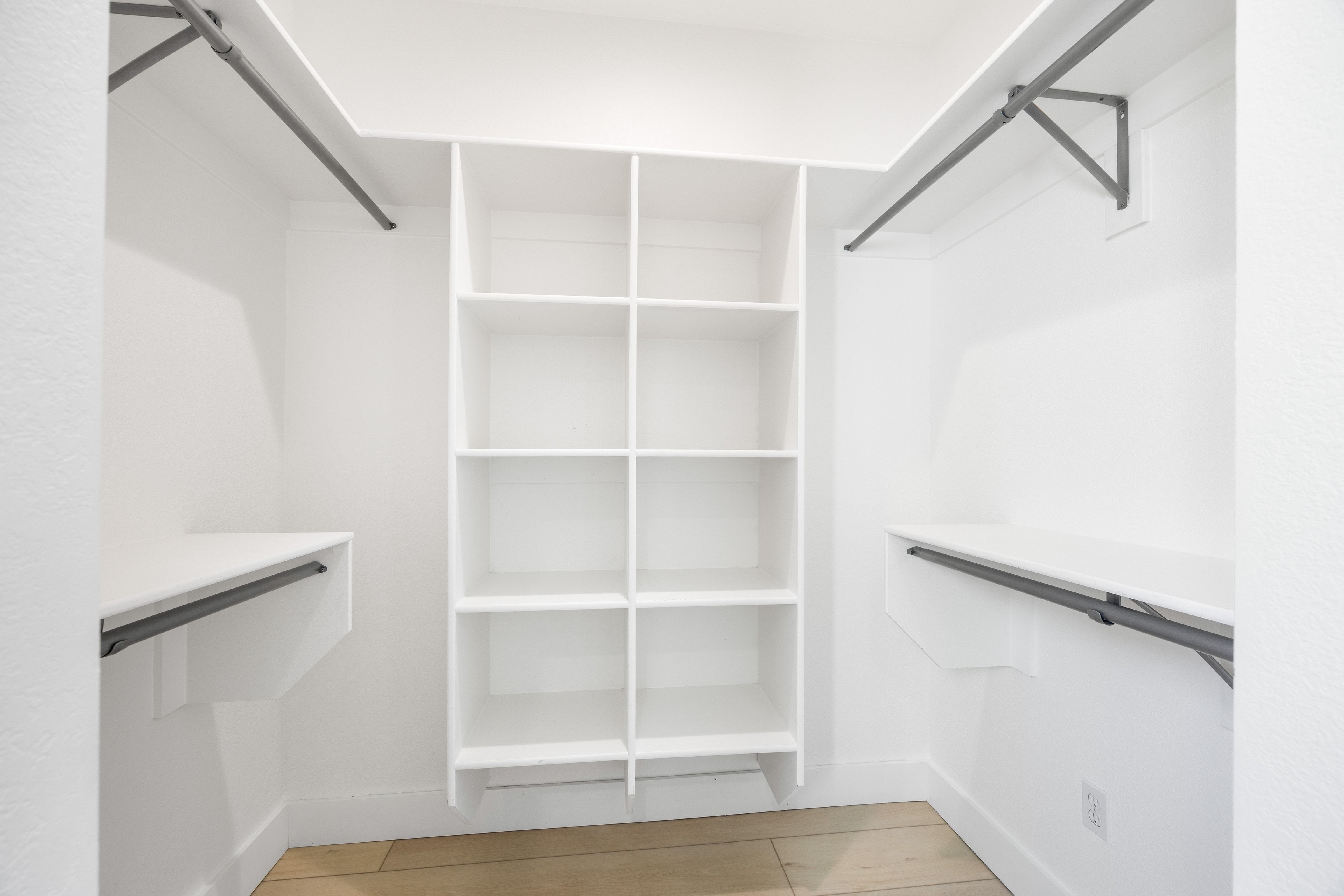 Walk-in closet featuring white built-in shelving, white walls, light wood-finish flooring, and metal hanging rods