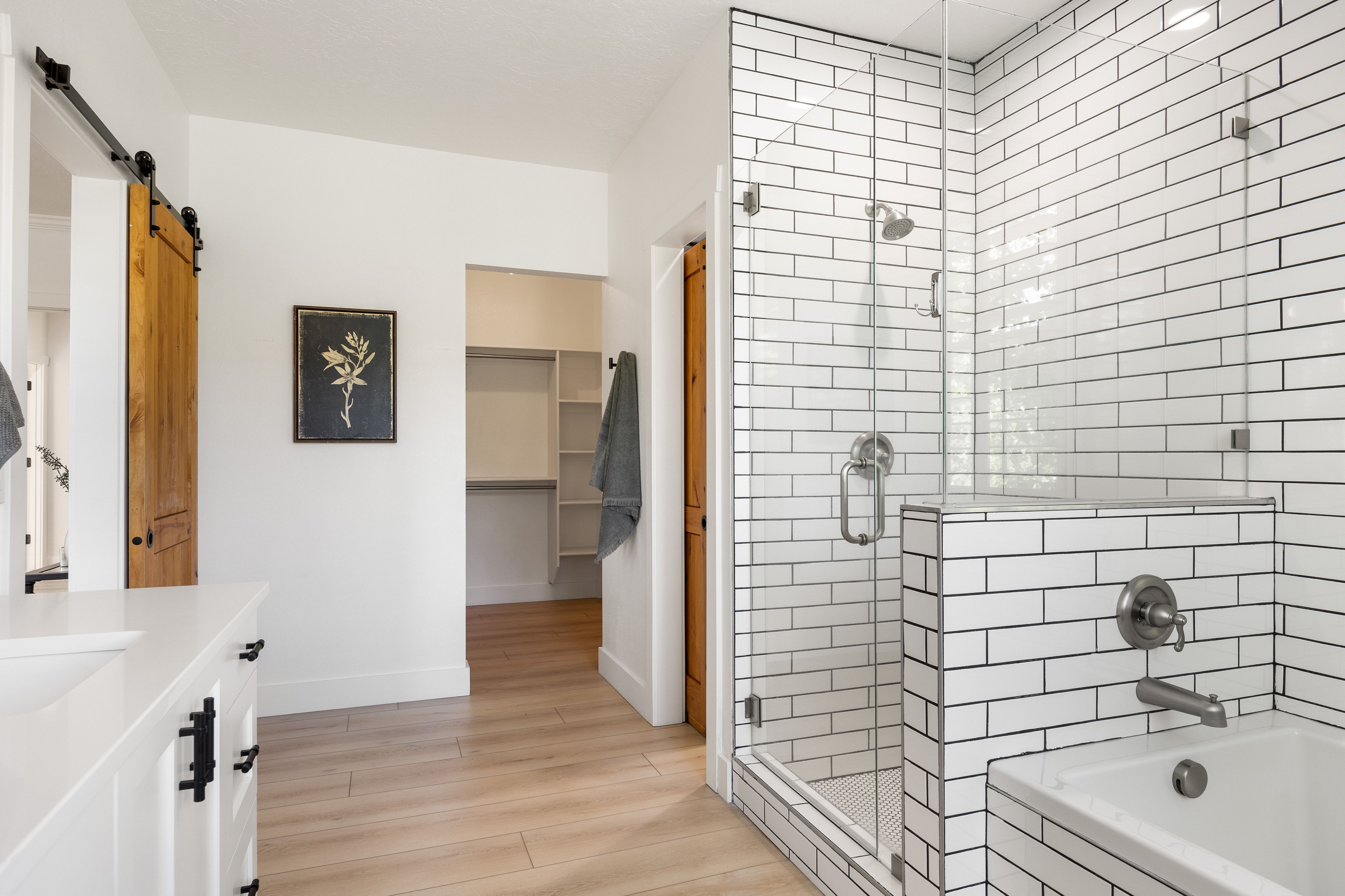 Bathroom featuring a glass-enclosed shower with subway tile surround, white soaking tub, and a vanity with white countertop and black hardware