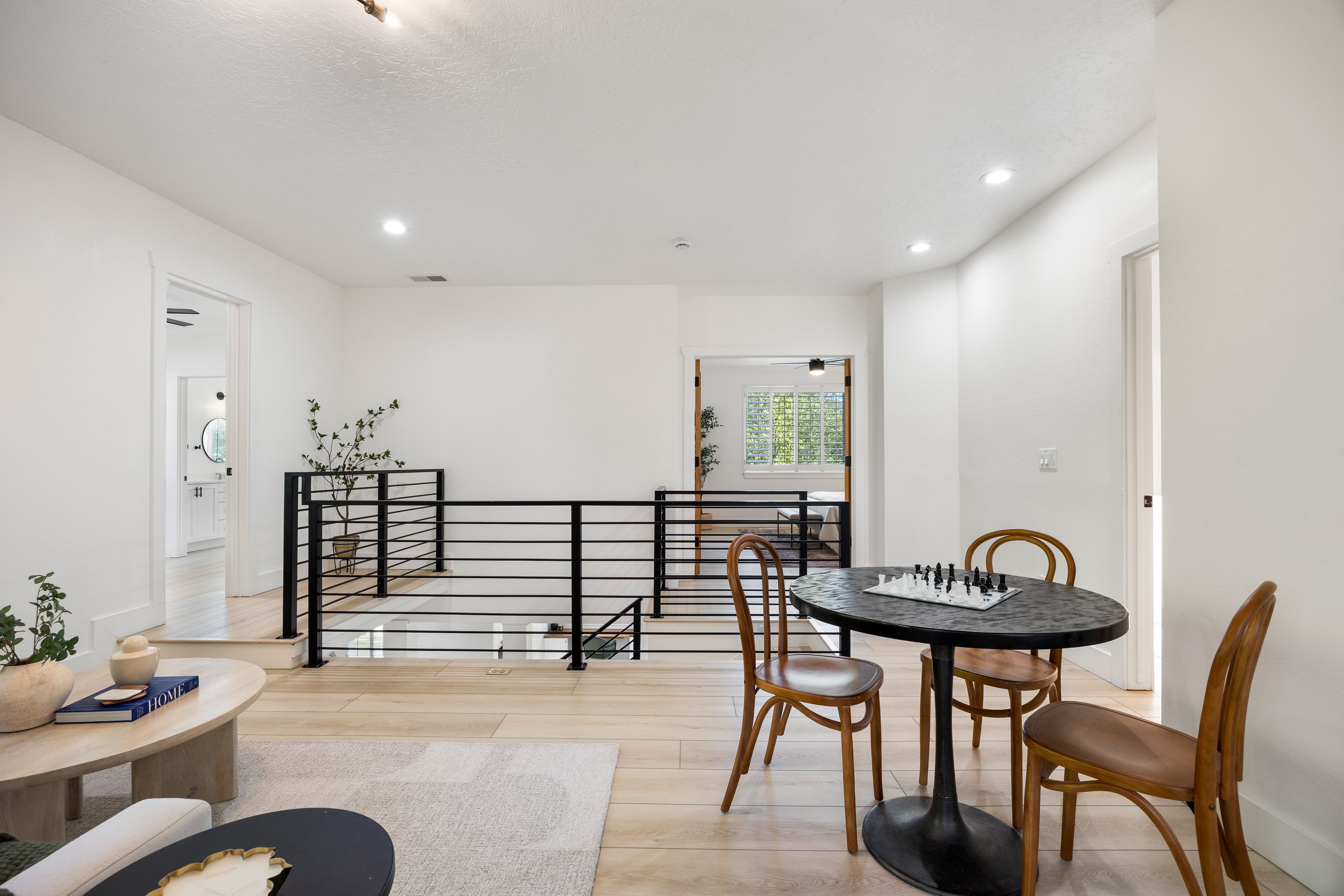 Upper-level landing featuring light wood-finish flooring, recessed lighting, and a contemporary black metal horizontal bar railing overlooking the lower level